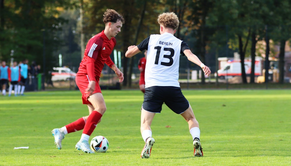 [{"clang_id":1,"value":"Zwei Fußballspieler auf grünem Rasen. Links rotes Trikot, rechts weiß-schwarzes Trikot mit Nummer 13 und \"Berlin\"-Schriftzug. Spieler verfolgen den Ball."}]