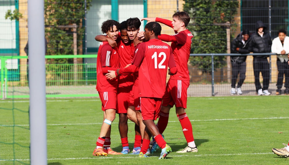 [{"clang_id":1,"value":"Fußballspieler in roten Trikots jubeln eng umschlungen auf einem Fußballfeld. Im Hintergrund eine grüne Hecke und Zuschauer."}]