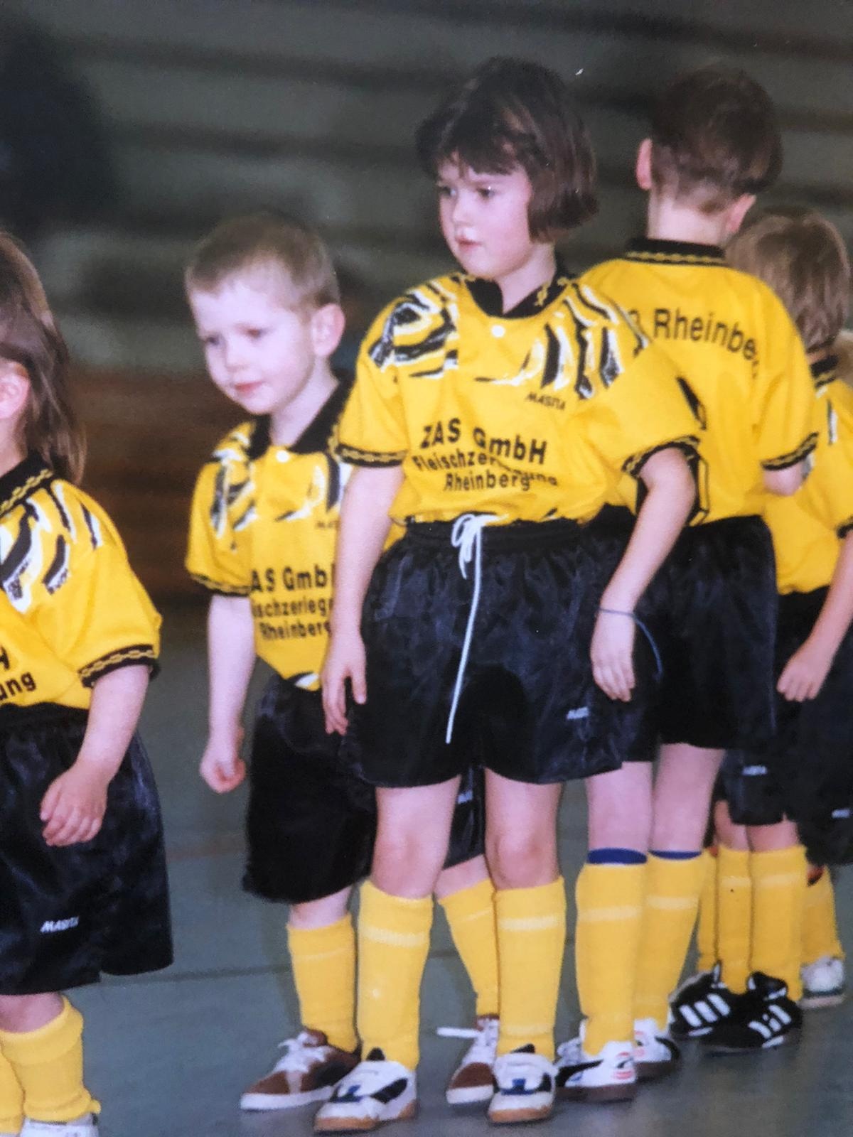 [{"clang_id":1,"value":"Eine Reihe junger Fussballspieler in gelben Trikots und schwarzen Shorts steht auf einem Hallenboden. Im Hintergrund weitere Spieler."}]