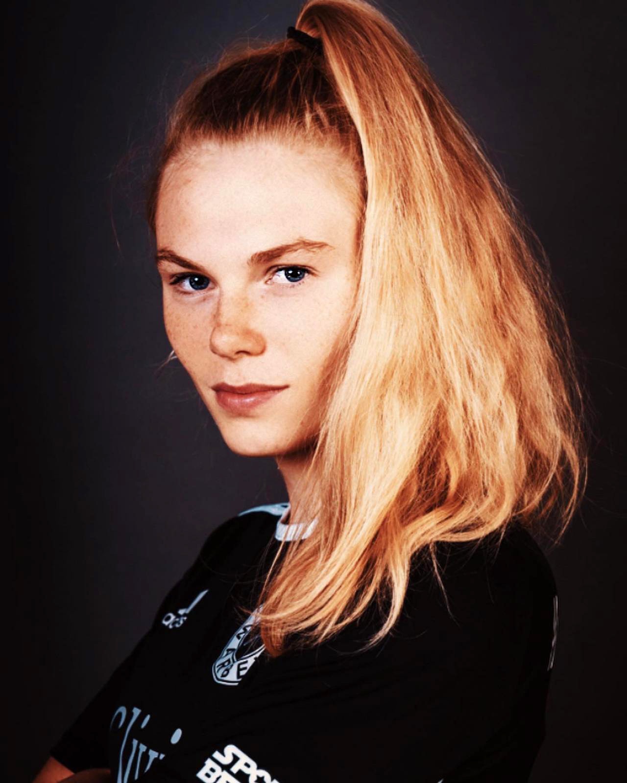 [{"clang_id":1,"value":"Rötlich-blondes Haar mit Pony, Gesicht mit Sommersprossen, dunkle Augen. Trägt schwarzes Sportshirt mit weißen Logos. Dunkler Hintergrund."}]