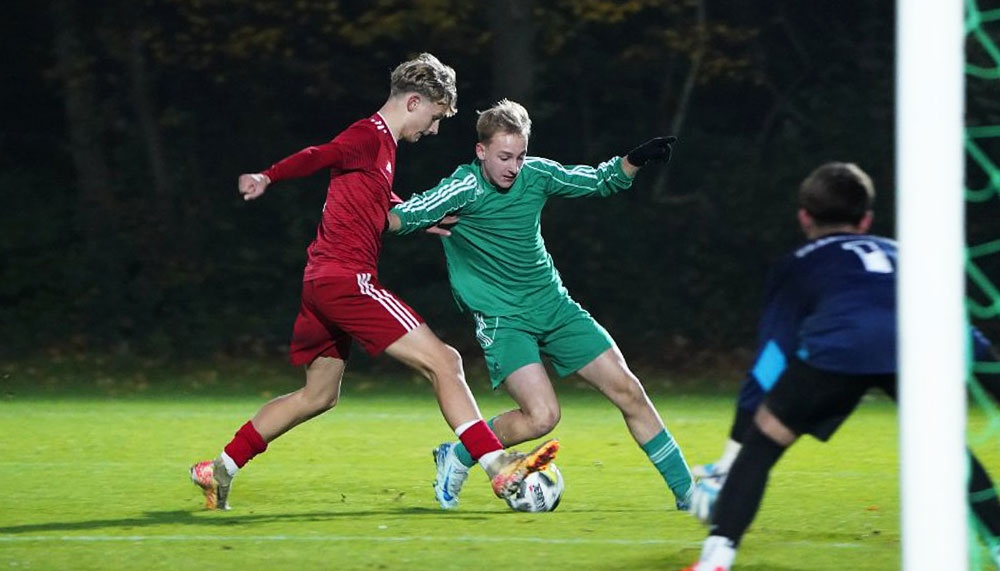 [{"clang_id":1,"value":"Fußballspiel: Spieler in Rot versucht, am Torwart in Grün vorbeizukommen. Im Hintergrund ein weiterer Spieler in Blau. Rasenplatz."}]