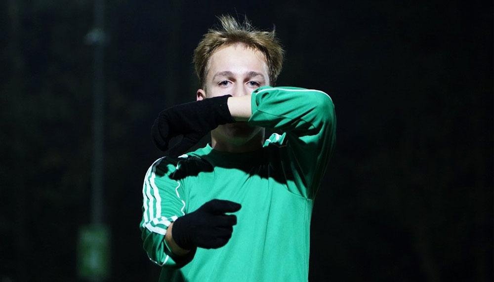 [{"clang_id":1,"value":"Fußballtorwart in grüner Sportbekleidung und schwarzen Handschuhen, bedeckt Gesicht mit den Händen. Dunkler Hintergrund mit Lichtmasten."}]