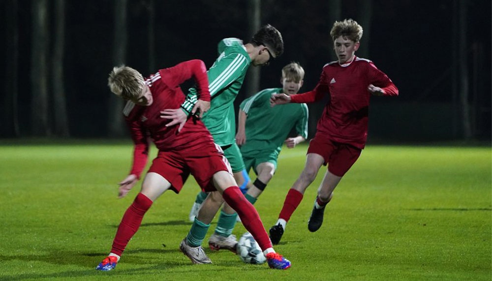 [{"clang_id":1,"value":"Fußballspiel: Drei Jugendliche in roten Trikots kämpfen um den Ball gegen zwei in grünen Trikots. Dunkler Hintergrund, vermutlich Abendspiel."}]