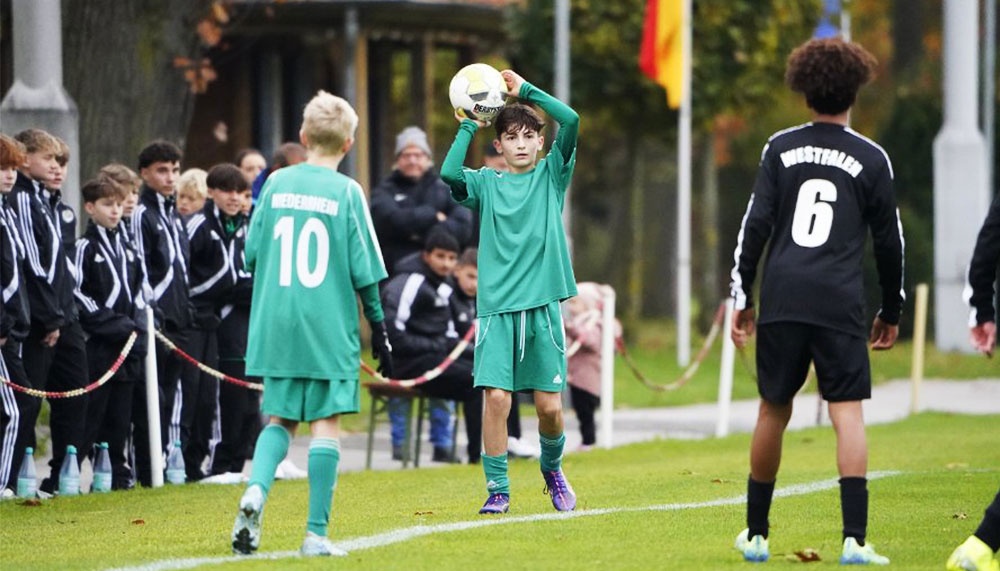[{"clang_id":1,"value":"Fußballspiel: Junge mit Ball wirft Einwurf, Gegenspieler direkt vor ihm. Im Hintergrund Zuschauer und Bankspieler in Vereinskleidung. Rasenplatz."}]