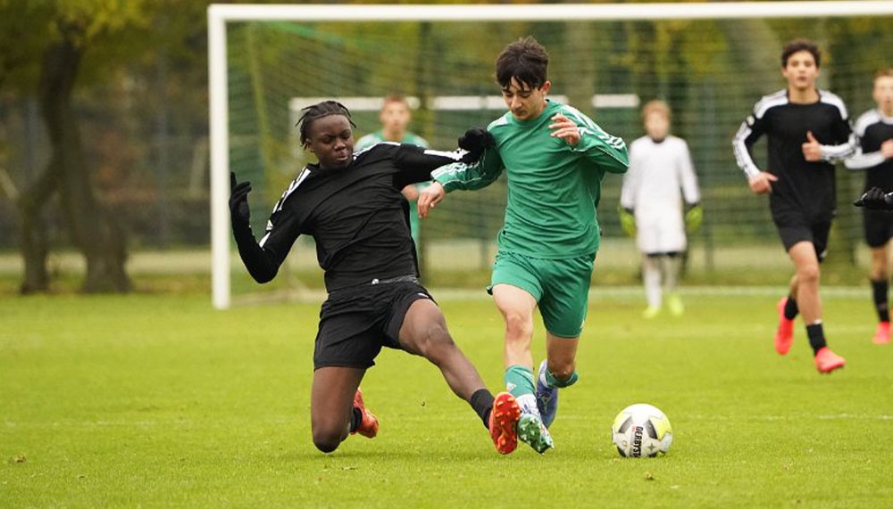 [{"clang_id":1,"value":"Fußballspiel: Zwei Spieler kämpfen um den Ball. Ein Spieler in Schwarz rutscht, der andere in Grün dribbelt. Im Hintergrund weitere Spieler und das Tor."}]
