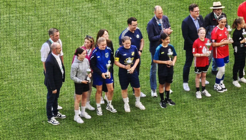 [{"clang_id":1,"value":"Gruppe von Menschen, darunter Kinder und Erwachsene, stehen auf einem Fußballfeld mit Trophäen in den Händen. Sie scheinen eine Preisverleihung zu feiern."}]