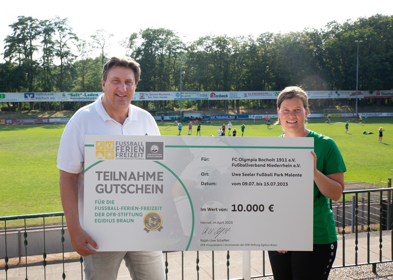 [{"clang_id":1,"value":"Zwei Personen mit einem Gutschein vor einem Fußballfeld. Der Gutschein ist für die Fussball-Ferienfreizeit des DFB-Stiftung Egidius Braun für FC Olympia Bocholt."}]