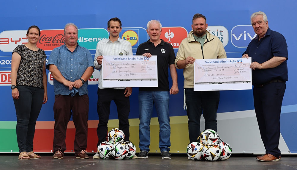 [{"clang_id":1,"value":"Fünf Männer stehen auf einer Bühne vor einem Werbebanner. Sie halten Schecks und Fußball-Dekorationen."}]