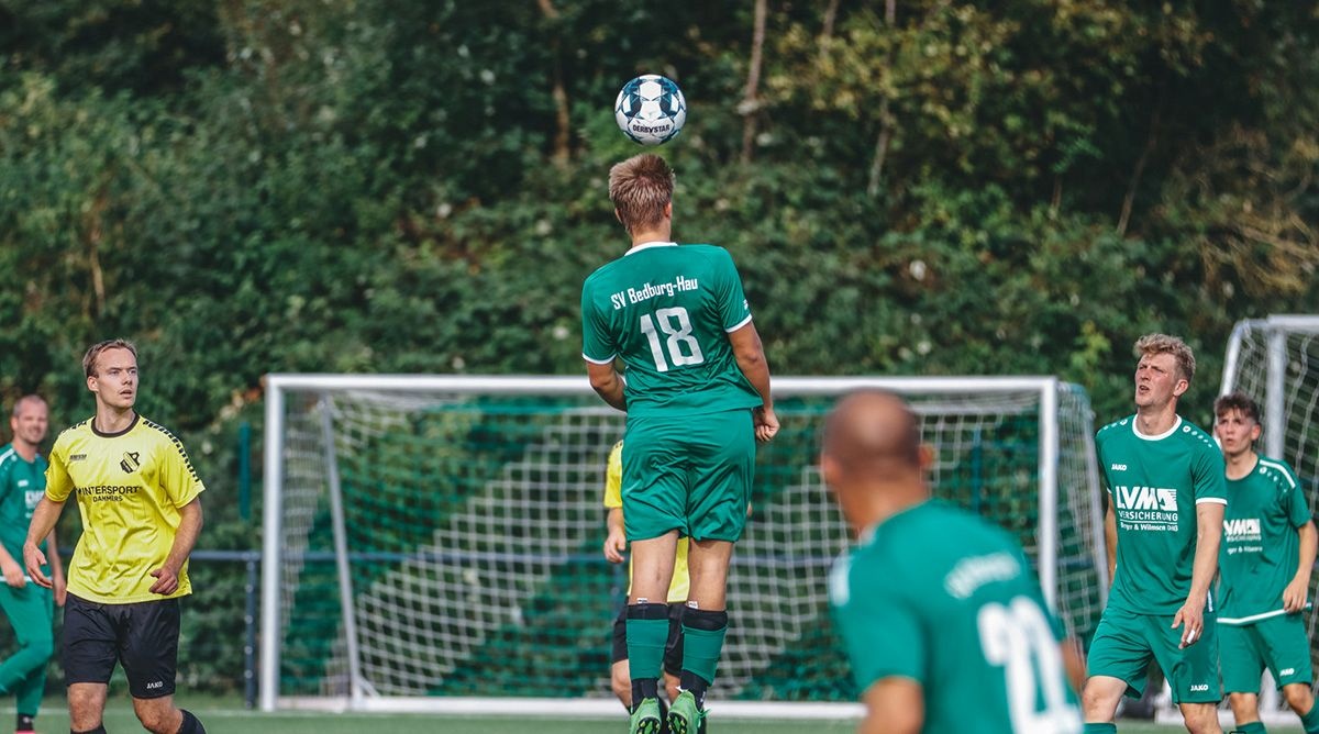 [{"clang_id":1,"value":"Fußballspieler mit Nummer 18 köpft Ball vor dem Tor. Im Hintergrund weitere Spieler in grün-weißen und gelben Trikots, sowie ein Fußballfeld mit Grün."}]