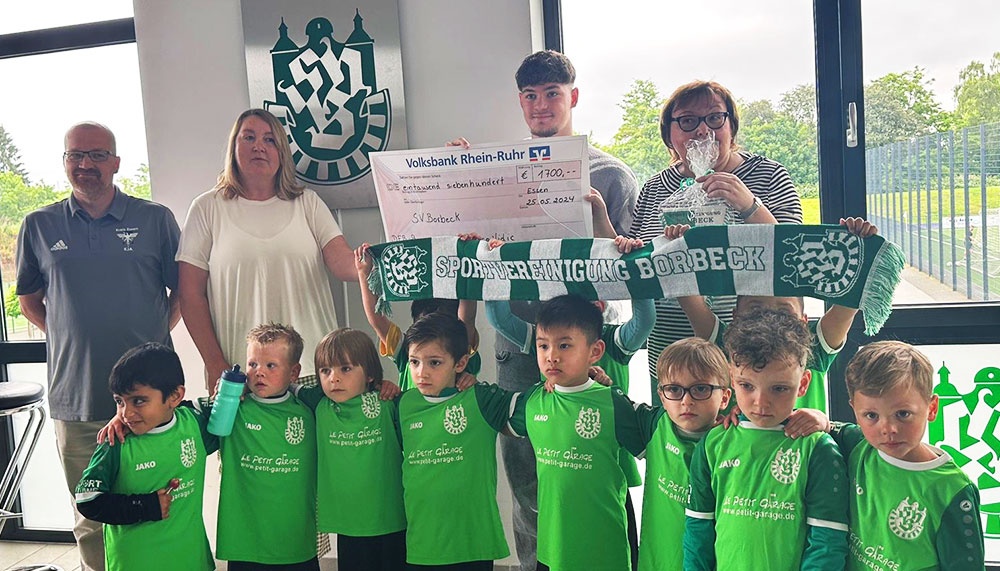 [{"clang_id":1,"value":"Fußballmannschaft mit Kindern in grünen Trikots präsentiert Scheck von Sponsor Volksbank Rhein-Ruhr. Erwachsene stehen dahinter."}]