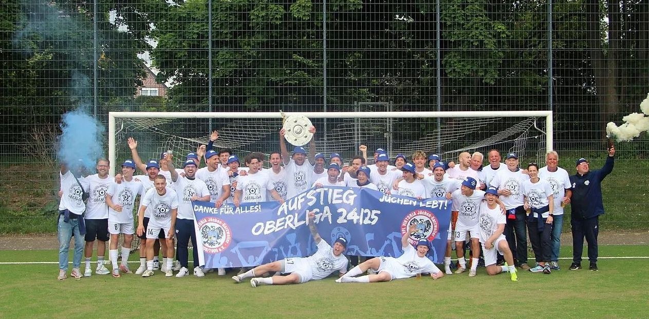 [{"clang_id":1,"value":"Fußballmannschaft mit Siegerpokal und Banner \"Aufstieg Oberliga 24/25\" auf grünem Rasen, umgeben von Zaun und Bäumen. Rauchbomben zünden."}]