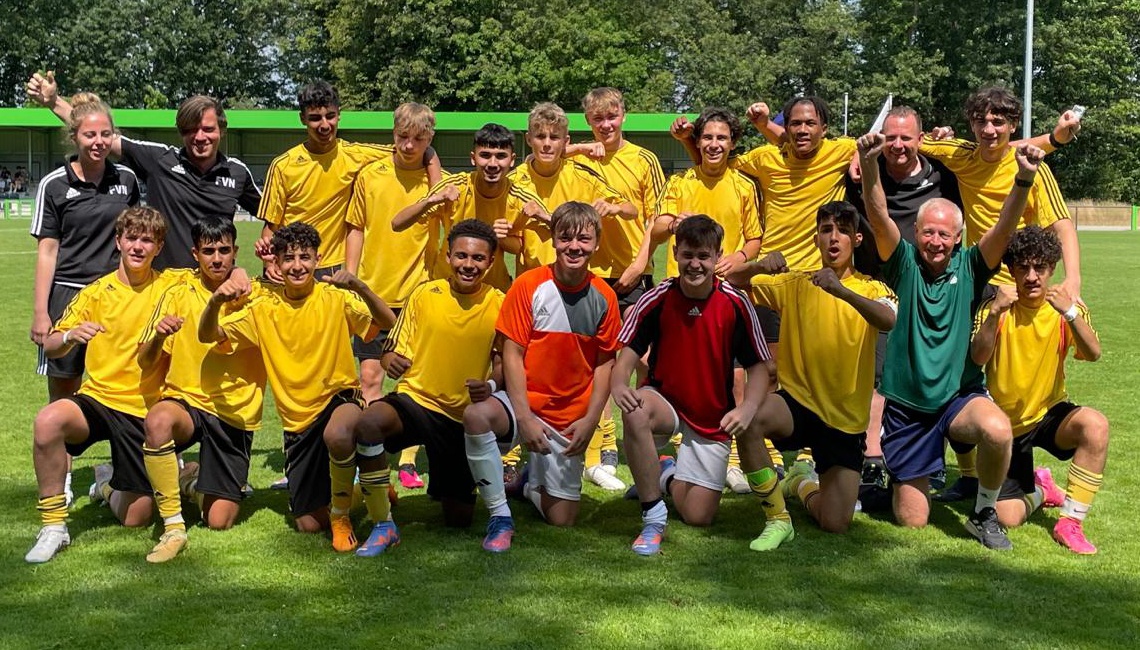 [{"clang_id":1,"value":"Fußballmannschaft in gelben Trikots kniet und steht auf grünem Rasen, einige Personen in Trainingsanzügen, im Hintergrund Gebäude und Bäume."}]
