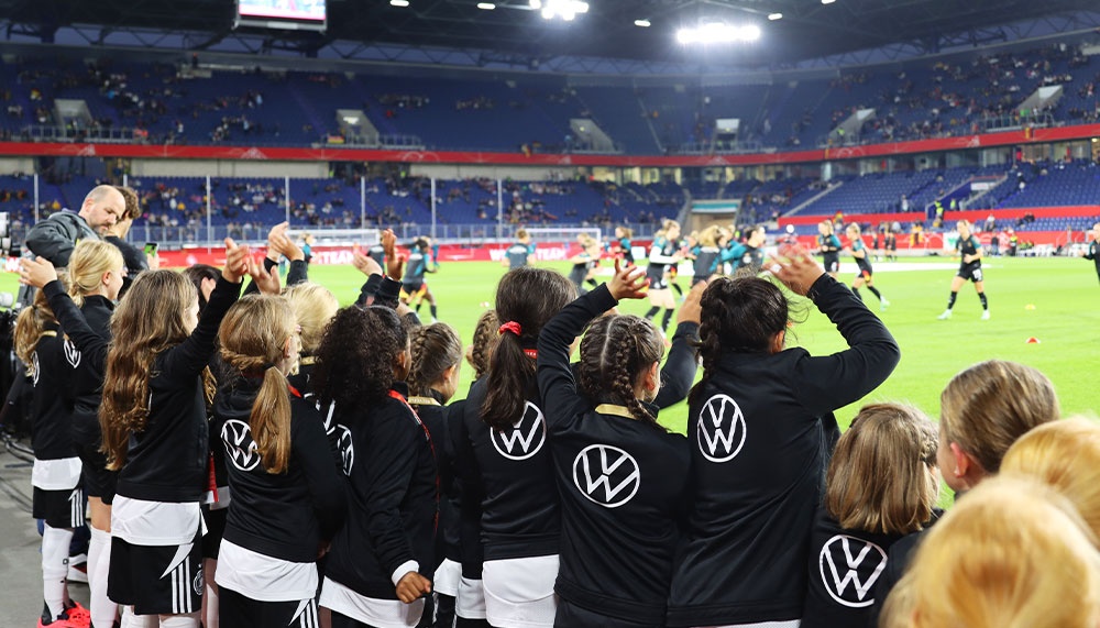 [{"clang_id":1,"value":"Fußballstadion: Eine Gruppe von jungen Sportlerinnen steht mit dem Rücken zum Betrachter in einem Kreis zusammen. Im Hintergrund das Spielfeld und Zuschauer."}]