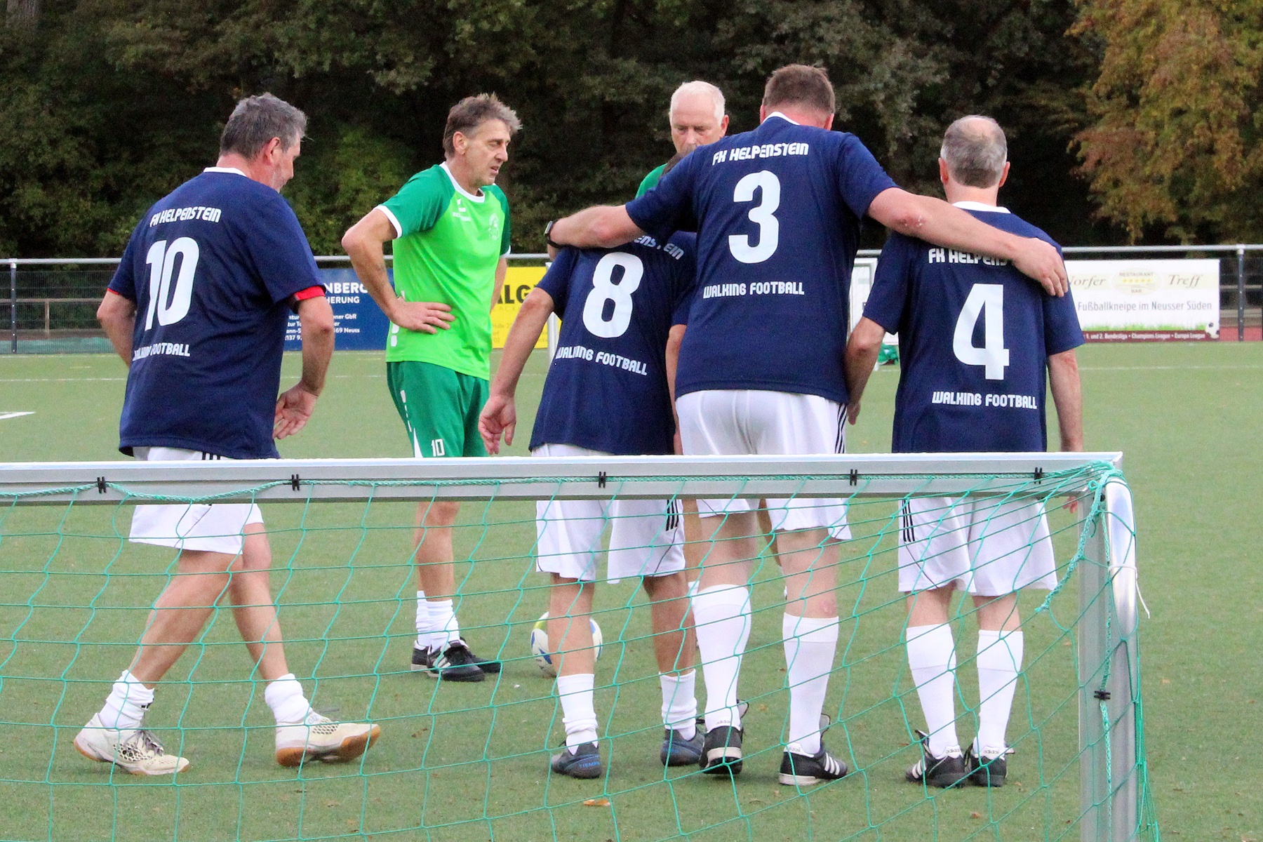 [{"clang_id":1,"value":"Fünf Männer in Sportkleidung stehen auf einem grünen Fußballfeld. Vier tragen blaue Trikots mit den Nummern 3, 4, 8 und 10, einer ein grünes Trikot. Sie scheinen zu diskutieren."}]