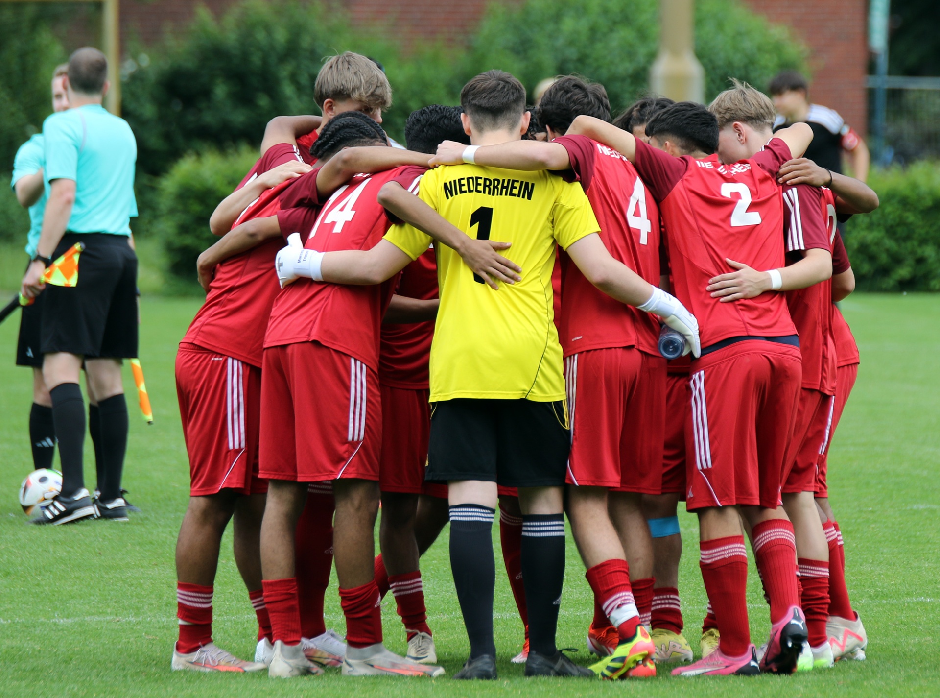 [{"clang_id":1,"value":"Fußballmannschaft in roten Trikots im Kreis, teilweise mit Nummernanzeige. Im Hintergrund Schiedsrichter und Zuschauer am Spielfeldrand."}]