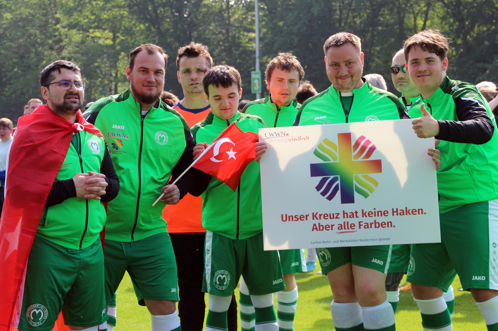 [{"clang_id":1,"value":"Fußballteam in grünen Trainingsanzügen mit türkischer Flagge und Spruchtafel: \"Unser Kreuz hat keine Haken. Aber alle Farben.\" Auf dem Rasen stehend."}]