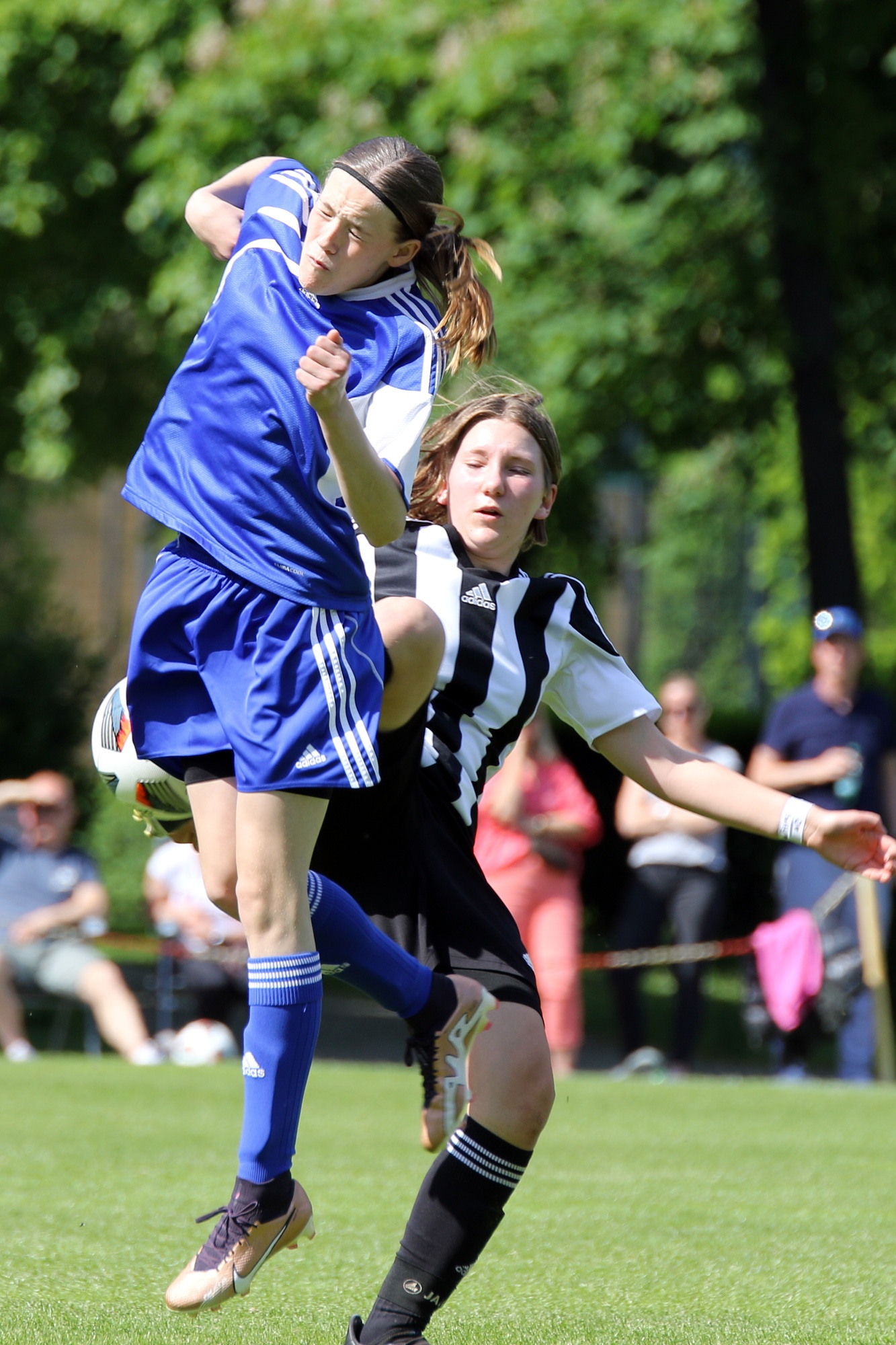 [{"clang_id":1,"value":"Zwei Fußballspielerinnen kämpfen um den Ball. Eine springt, die andere wehrt ab. Hinter ihnen steht Publikum und Grünfläche."}]
