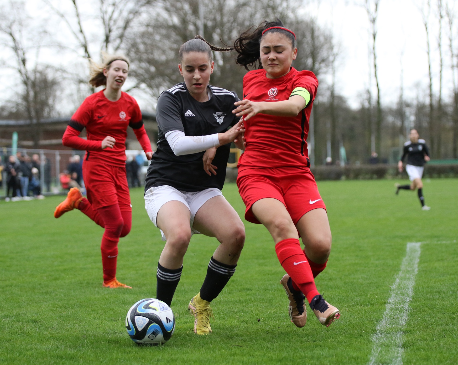 [{"clang_id":1,"value":"Fußballspiel: Zwei Spielerinnen in Rot und Schwarz kämpfen um den Ball. Im Hintergrund weitere Spielerinnen und Zuschauer am Spielfeldrand."}]