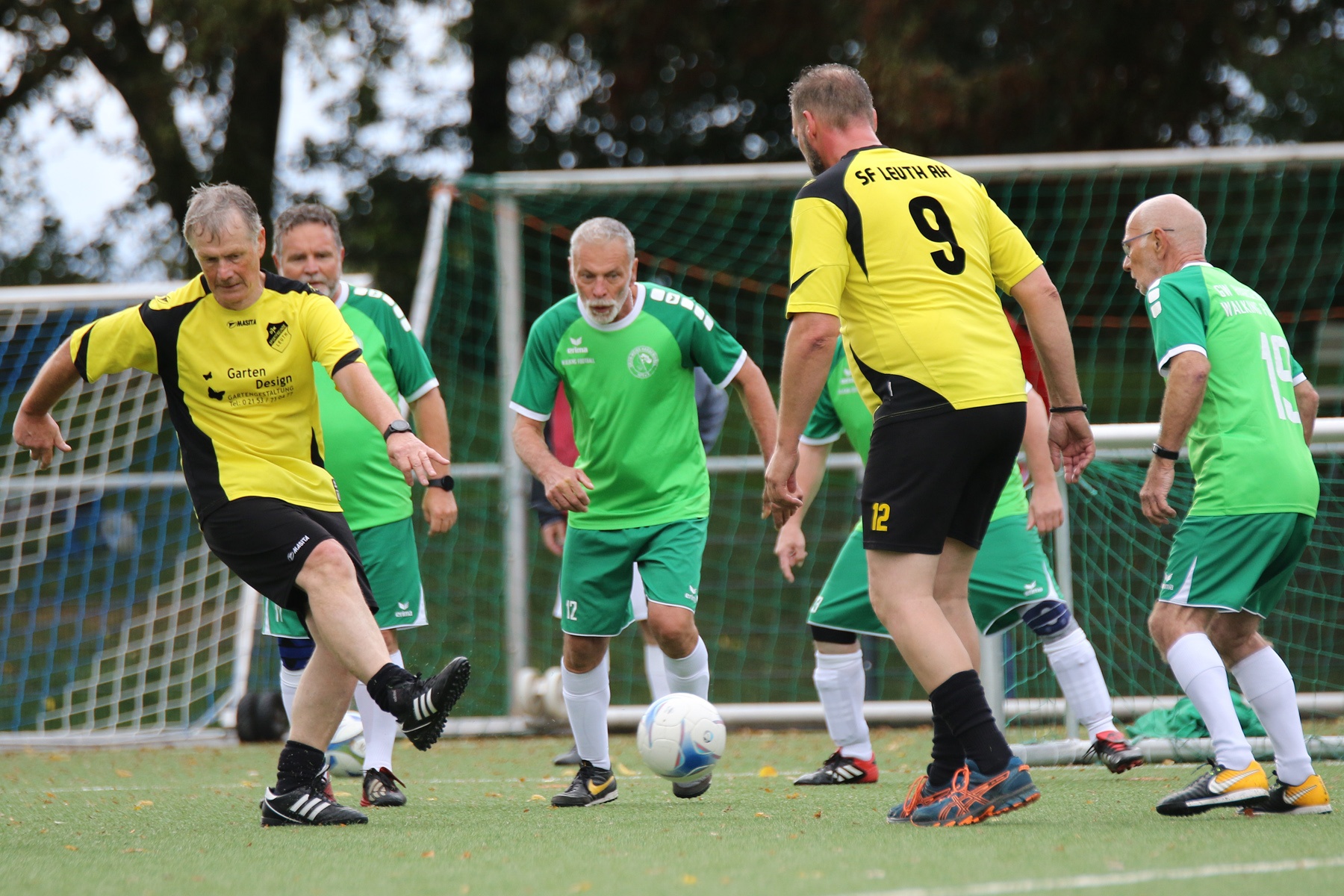 [{"clang_id":1,"value":"Fußballspiel: Männer mittleren Alters in gelben und grünen Trikots kämpfen um den Ball auf einem Rasenplatz. Im Hintergrund ein Fußballtor."}]