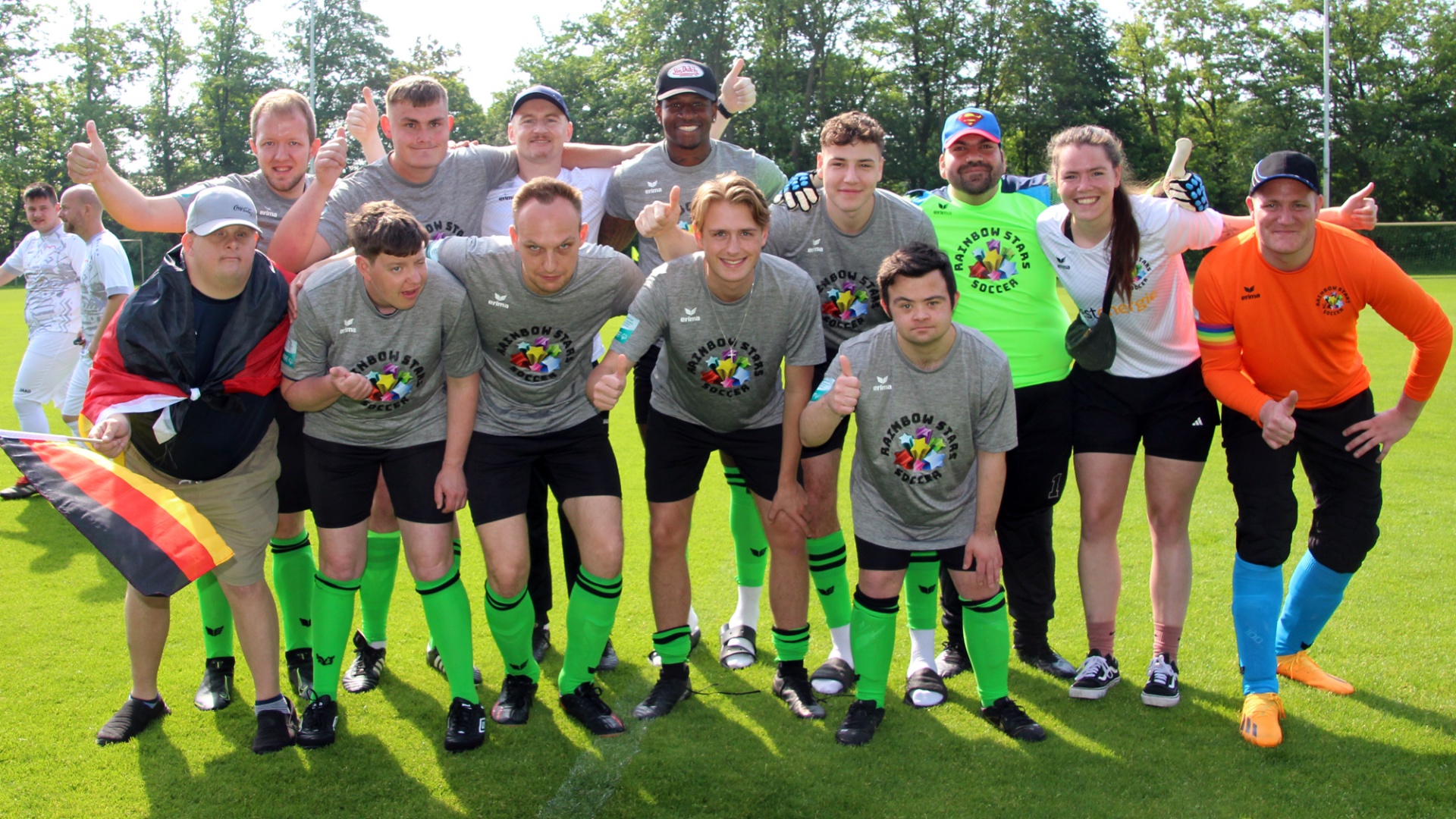 [{"clang_id":1,"value":"Fußballmannschaft steht lächelnd auf grünem Rasen. Die Spieler tragen graue Shorts, schwarze T-Shirts mit Logo und neon-grüne Socken. Einige halten die Regenbogenflagge hoch."}]