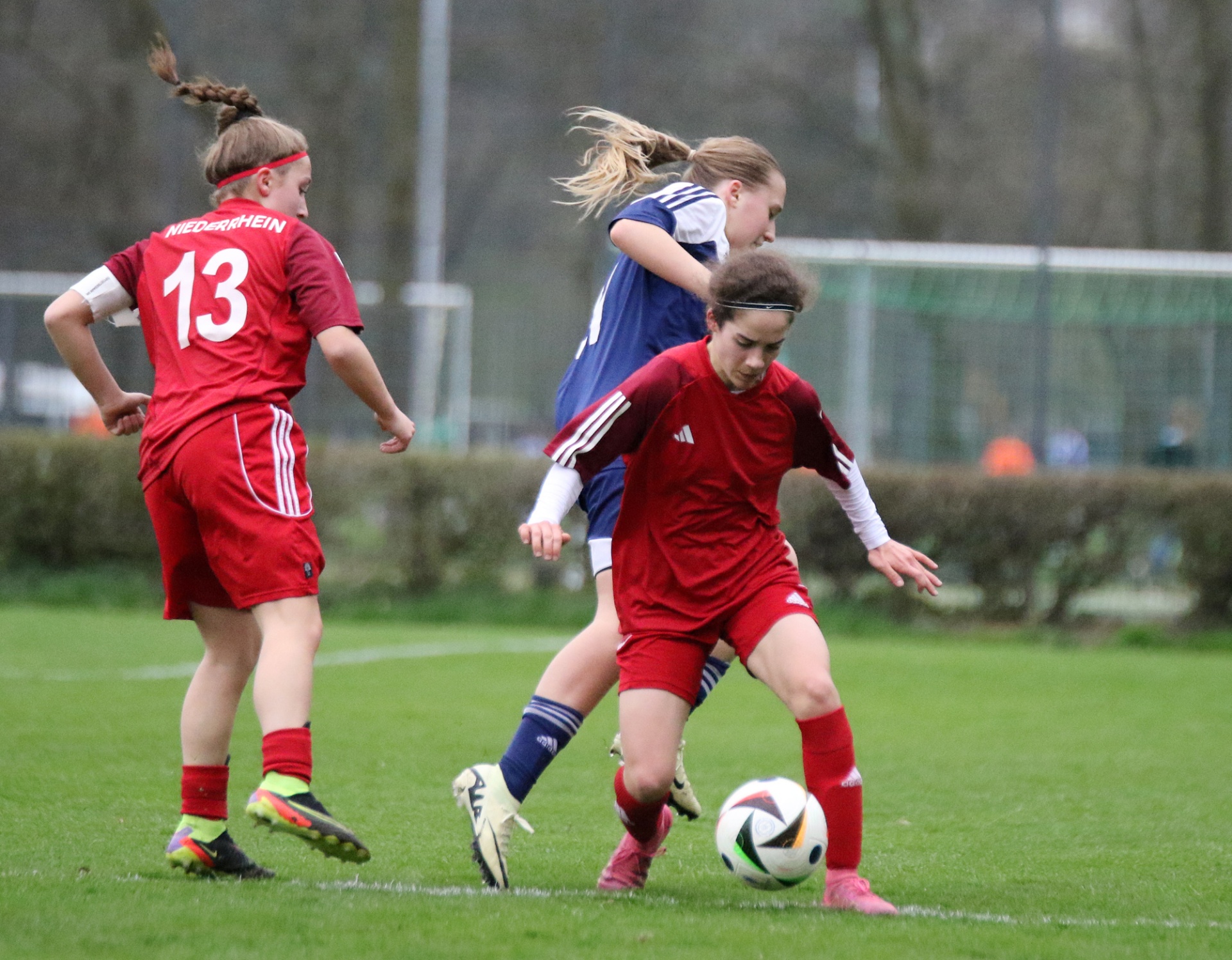 [{"clang_id":1,"value":"Zwei Fußballspielerinnen kämpfen um den Ball auf einem Rasenplatz. Links trägt eine Spielerin Trikotnummer 13, rechts blaues Trikot."}]