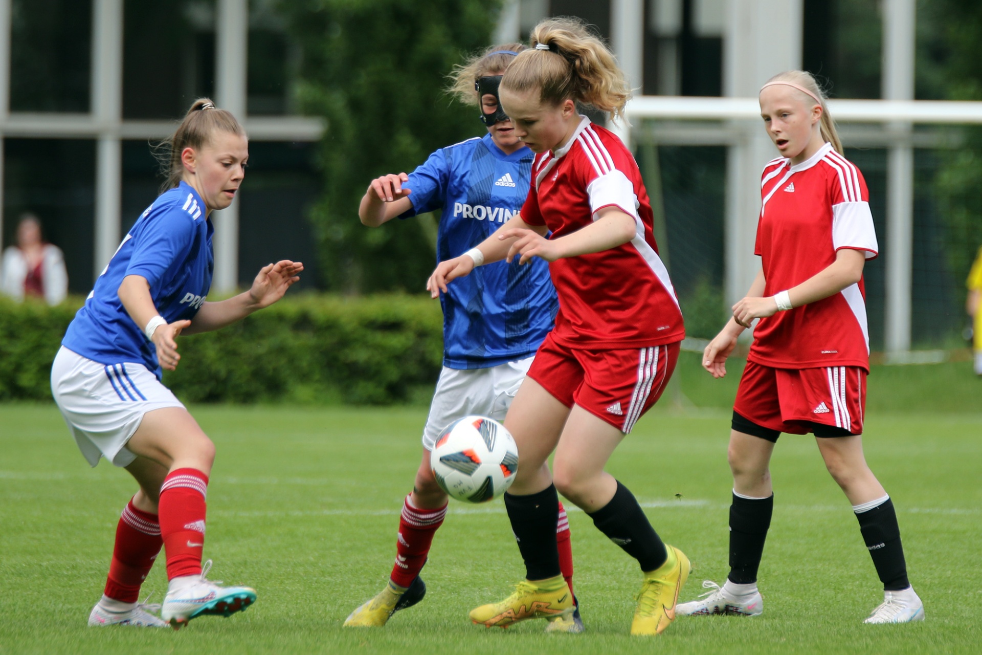 [{"clang_id":1,"value":"Drei junge Fußballspielerinnen auf grünem Rasen. Links blaues Trikot, Mitte blaues Trikot mit Ball, rechts rotes Trikot."}]