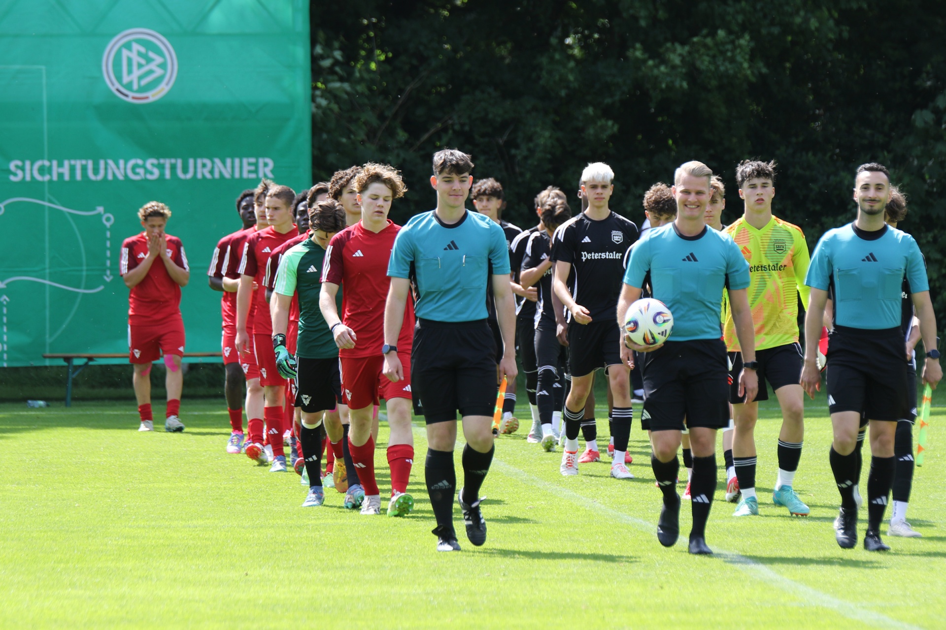 [{"clang_id":1,"value":"Fußballspiel: Zwei Mannschaften mit verschiedenen Trikots stehen sich auf einem Rasenplatz gegenüber. Im Hintergrund eine grüne Werbeplane mit Logo und Text."}]