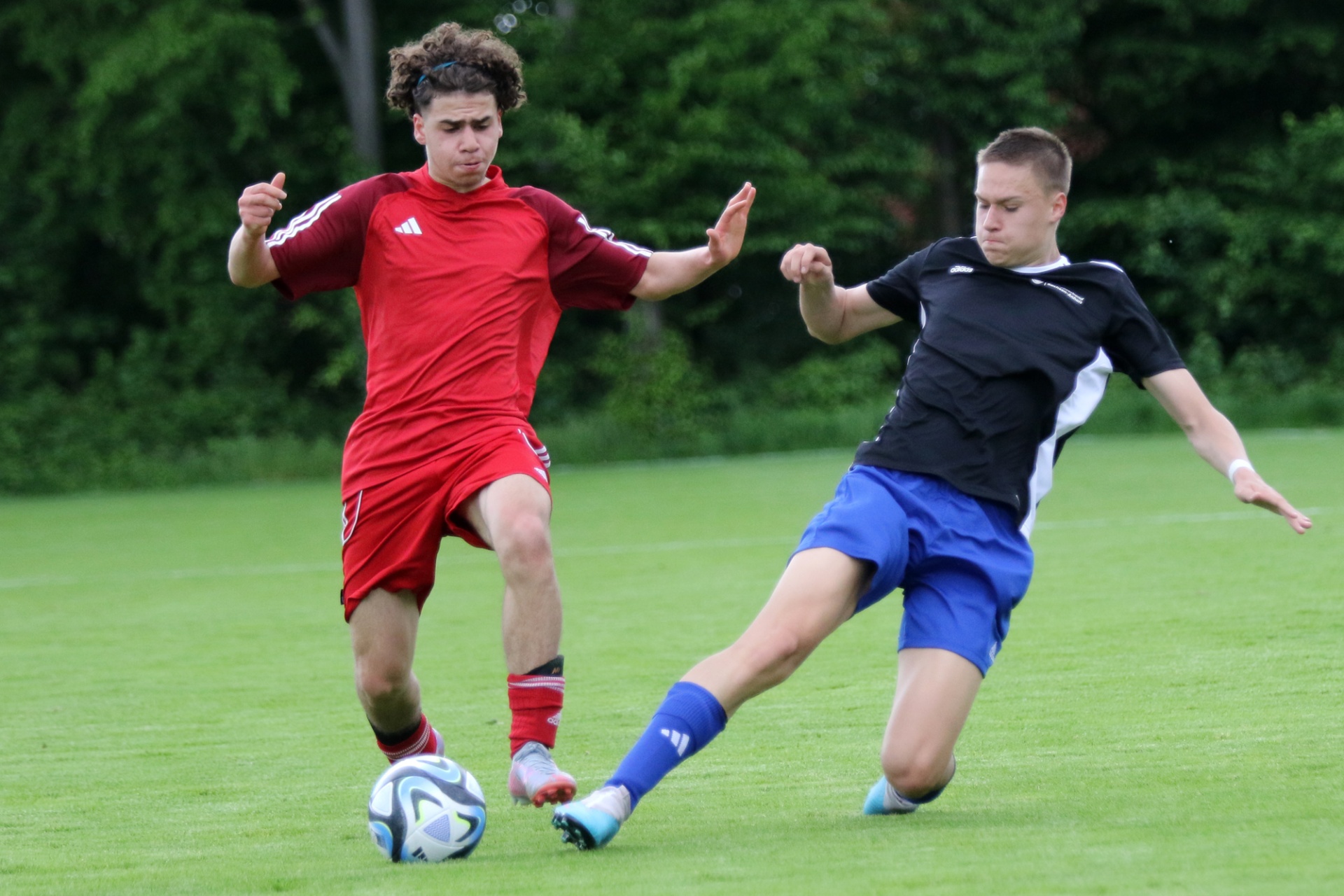 [{"clang_id":1,"value":"Zwei Fußballspieler auf grünem Rasen: Links ein Spieler in Rot, rechts in Schwarz-Blau. Der Rote spielt den Ball, der andere versucht ihn zu blocken."}]