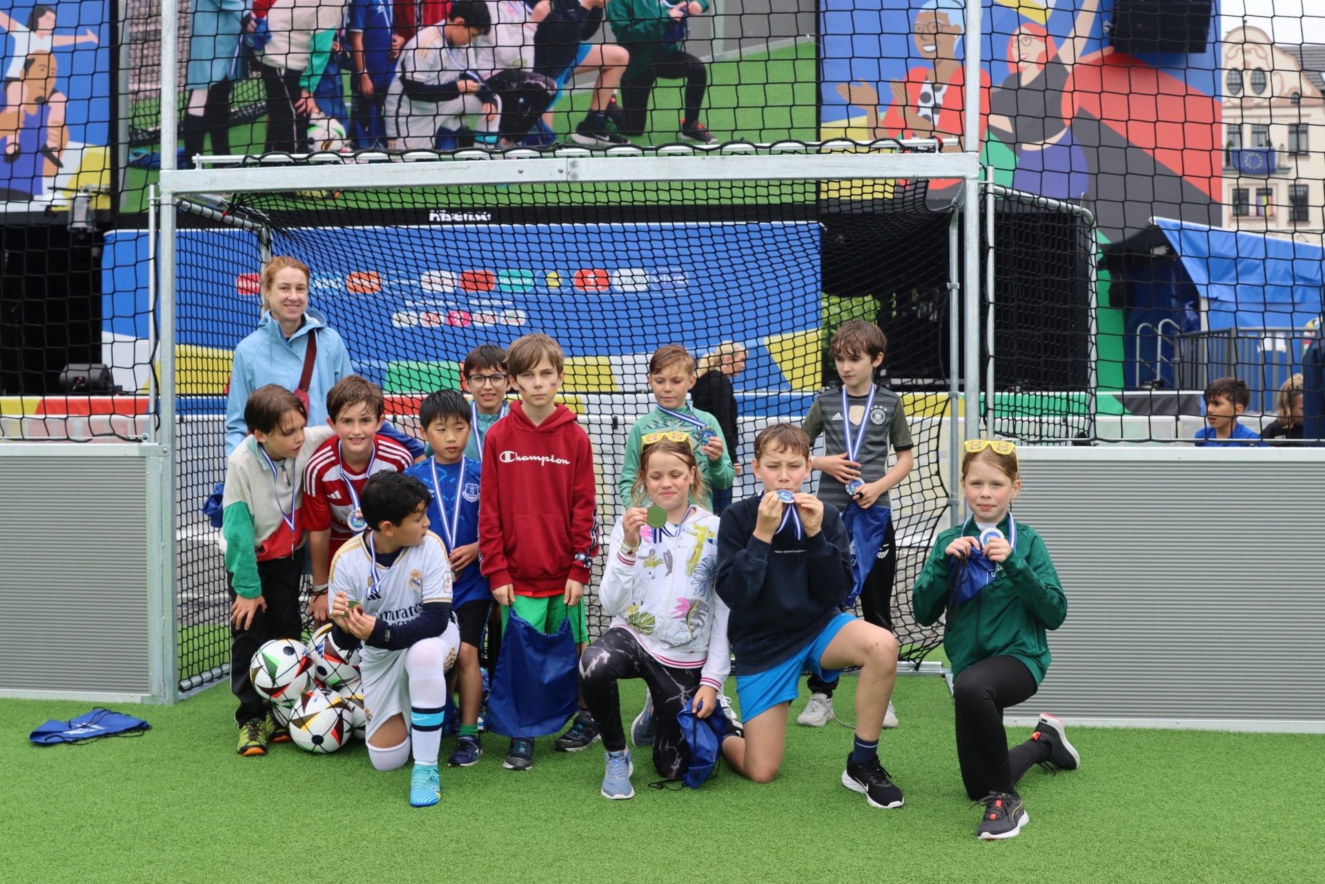 [{"clang_id":1,"value":"Fußballmannschaft mit Kindern und Betreuern posiert vor einem Fußballtor auf einem Kunstrasenplatz. Alle tragen Medaillen."}]