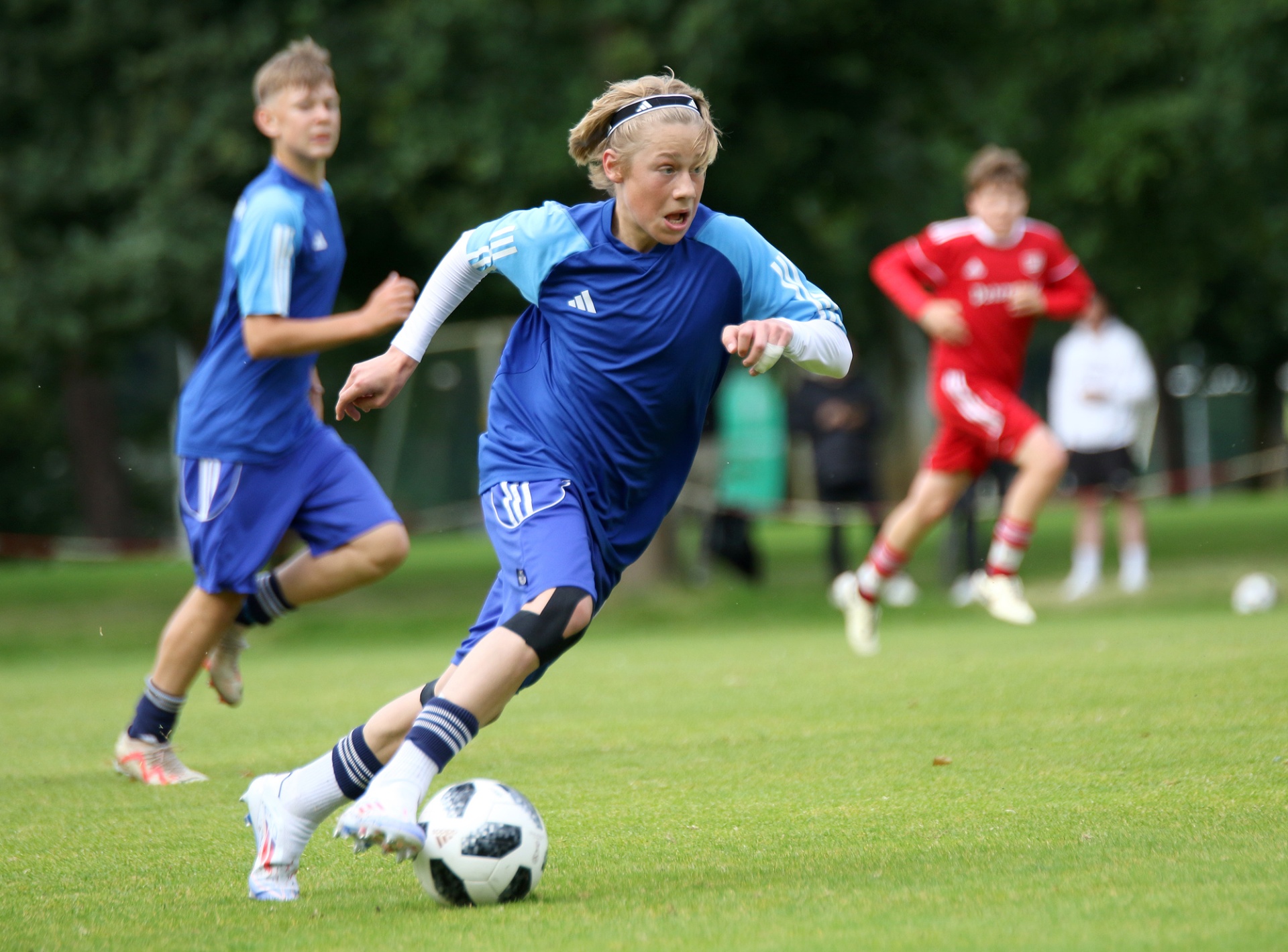 [{"clang_id":1,"value":"Junge Fußballspieler auf grünem Rasen während eines Spiels. Ein Spieler in blau dribbelt den Ball, dahinter und gegenüber weitere Spieler in blau und rot."}]
