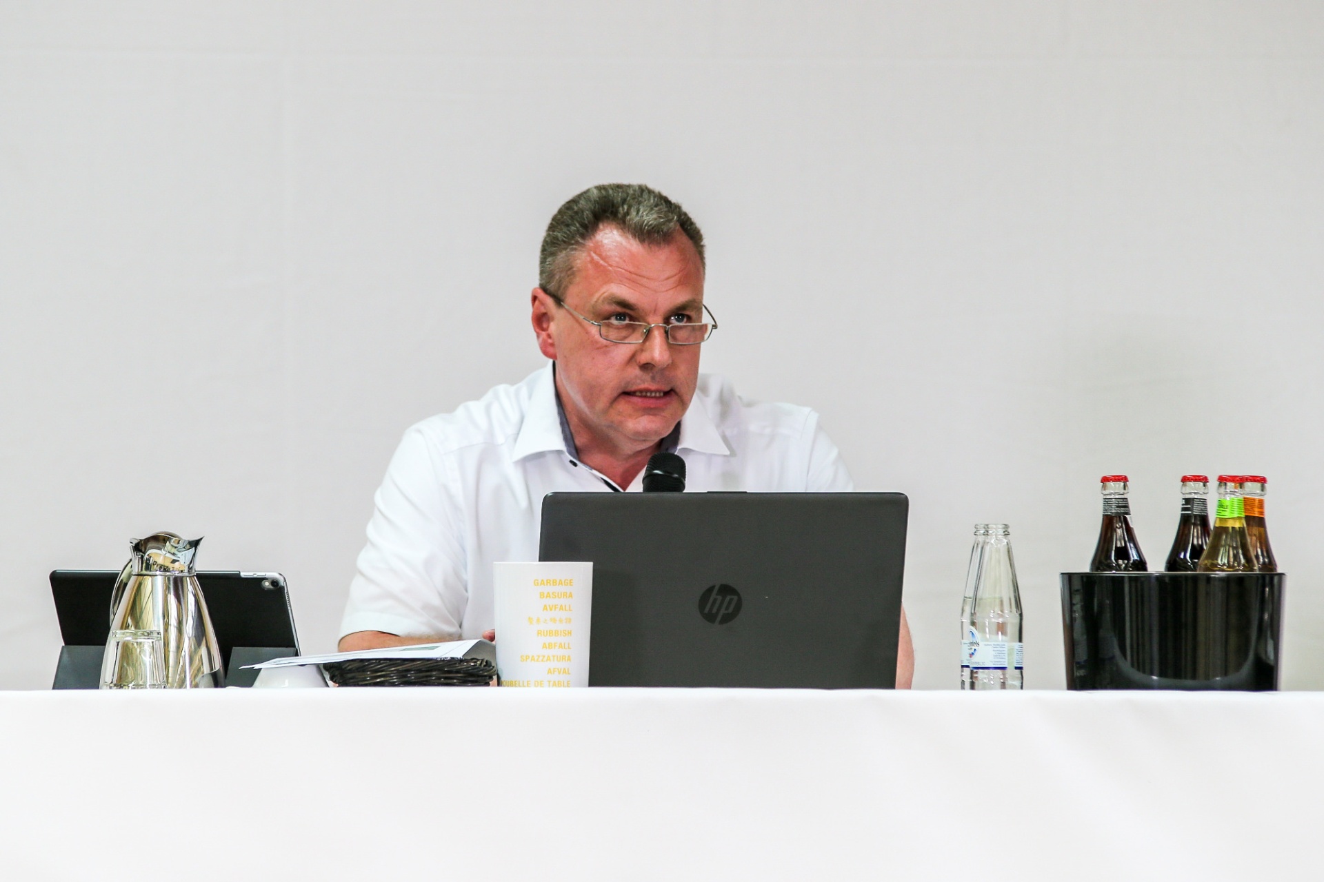 [{"clang_id":1,"value":"Mann mit Brille sitzt an einem Tisch vor Laptop und Papierstapel. Wassergläser und Getränkeflaschen stehen daneben. Helles Büro."}]