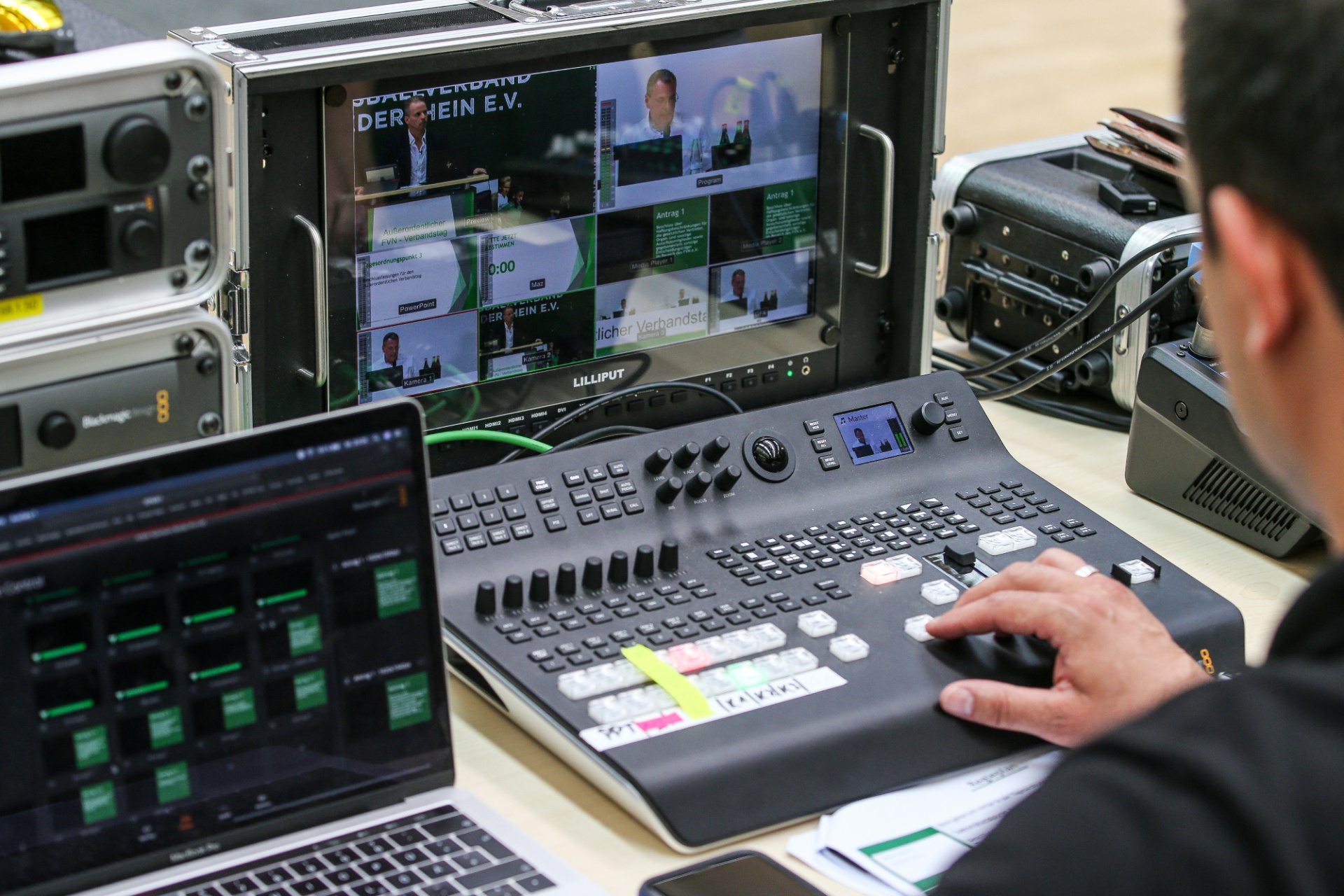 [{"clang_id":1,"value":"Mann bedient Videomischpult mit mehreren Monitoren. Auf den Monitoren sind Videobilder und Texte zu sehen. Rack mit technischem Equipment im Hintergrund."}]