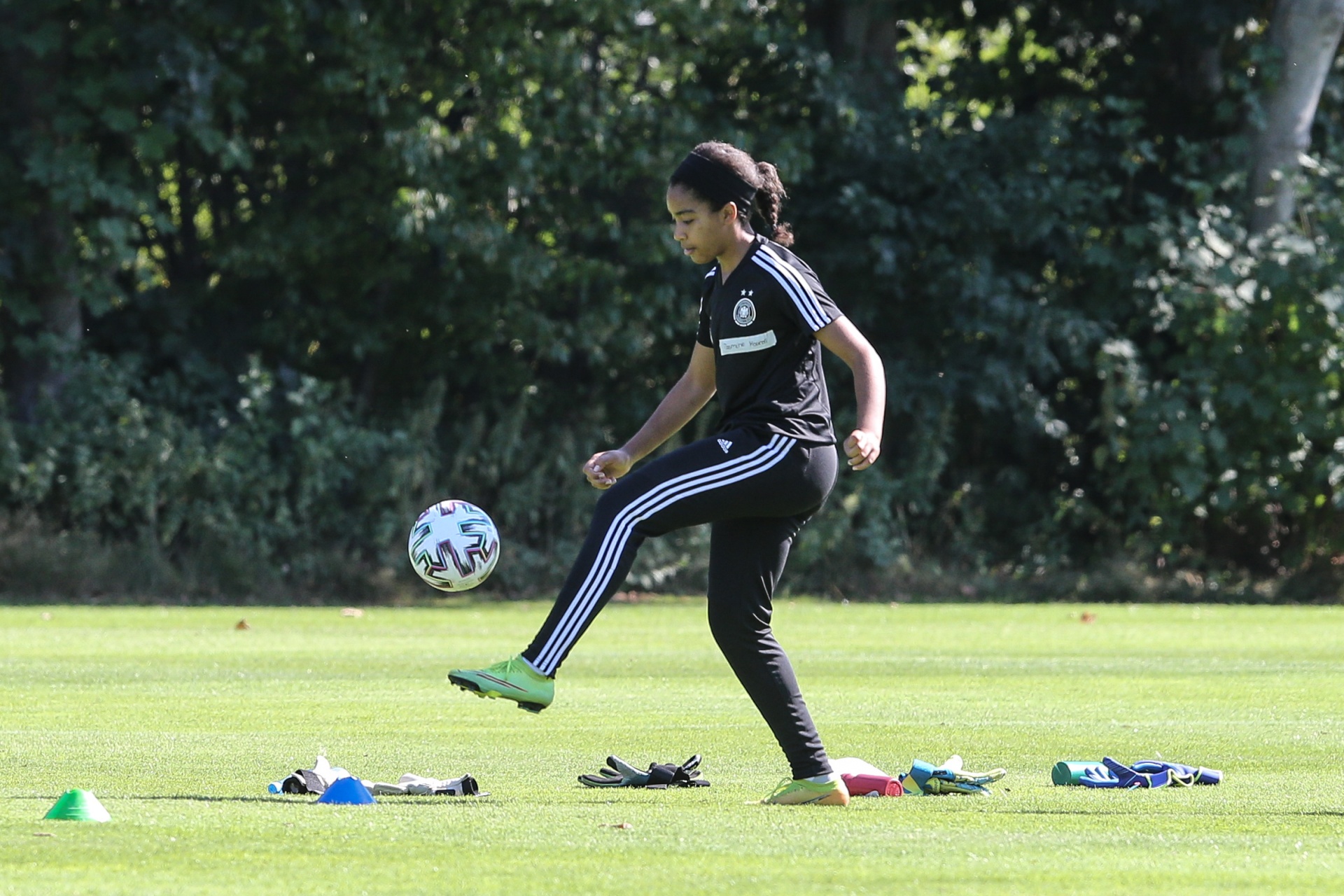 [{"clang_id":1,"value":"Junge Fußballerin mit dunklen Haaren dribbelt auf einer grünen Wiese mit einem Fußball. Im Hintergrund Bäume. Trainingsmarkierungen am Boden."}]