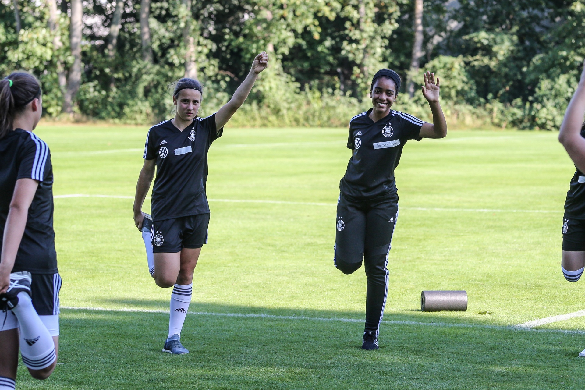 [{"clang_id":1,"value":"Fußballspielerinnen auf grünem Rasen trainieren. Zwei Spielerinnen im schwarzen Trainingsanzug gestikulieren. Hintergrund: Bäume."}]
