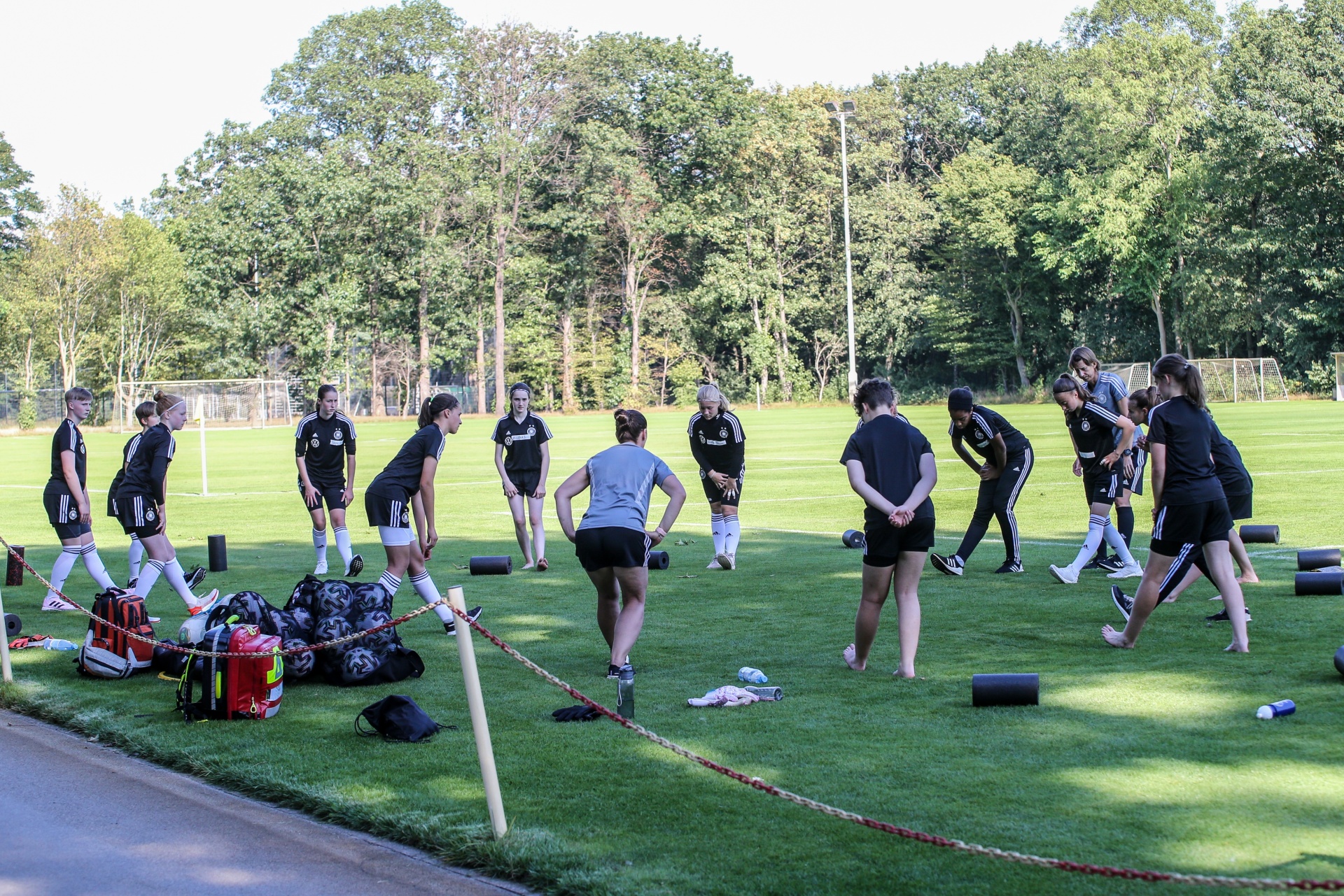 [{"clang_id":1,"value":"Fußballspielerinnen im Trainingslager. Gruppe dehnt auf grünem Rasen, Trainingsutensilien daneben. Hintergrund: Bäume und Fußballtor."}]