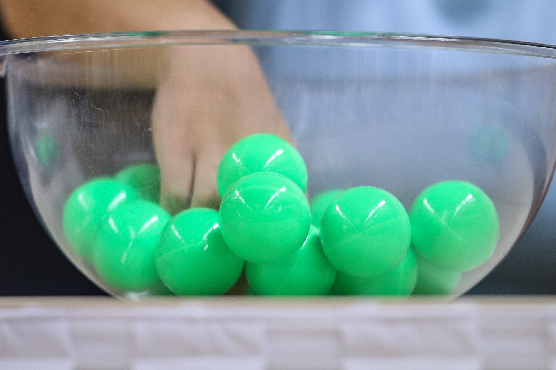 [{"clang_id":1,"value":"Grüne Plastikkugeln in einer transparenten Schüssel. Eine Hand greift in die Kugeln. Heller Hintergrund."}]