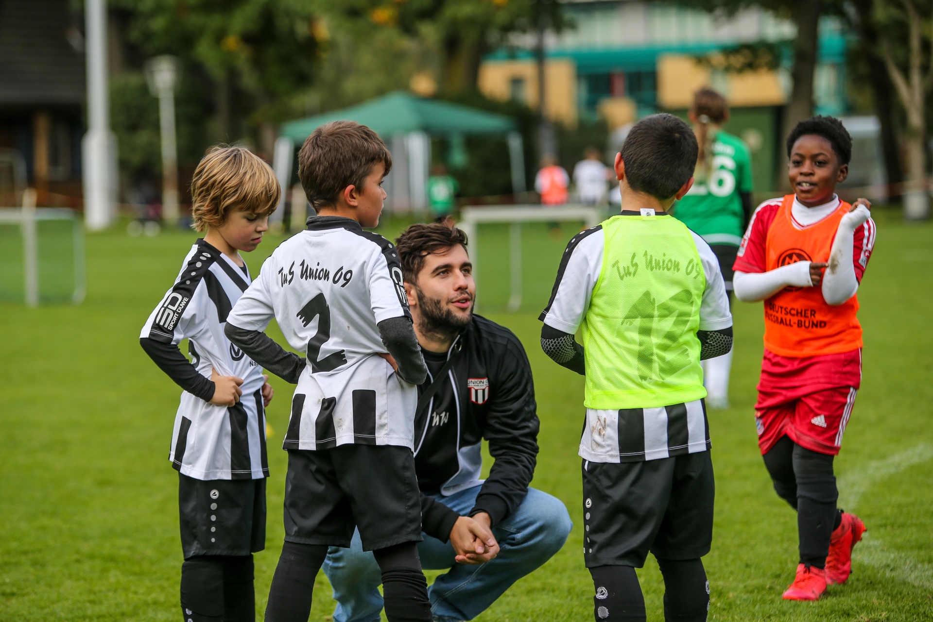 [{"clang_id":1,"value":"Fußballtraining Jugend: Trainer spricht mit vier Jungen auf Grünfläche. Spieler tragen Vereinskleidung schwarz-weiß bzw. gelb, ein Junge rote Trikots."}]