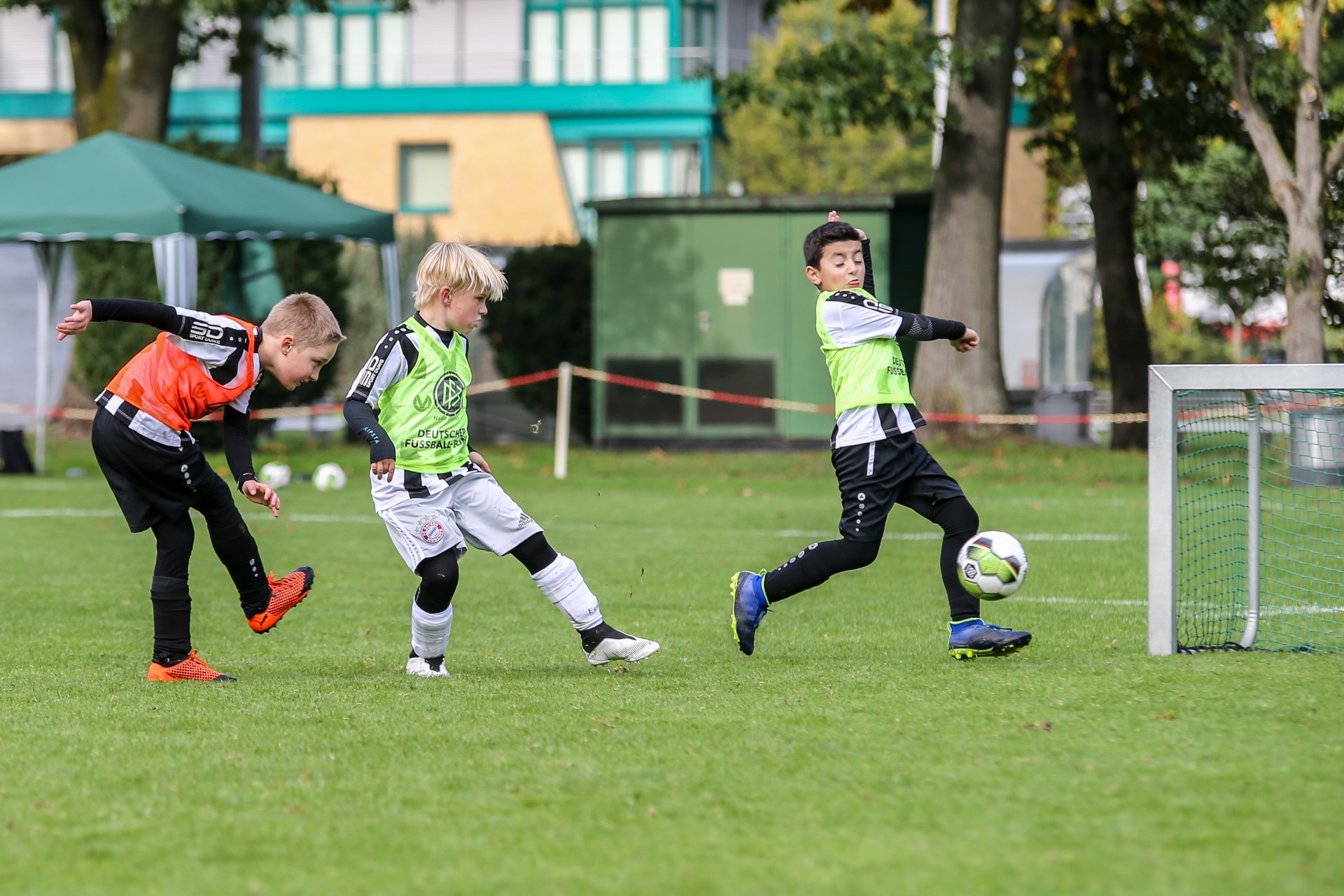 [{"clang_id":1,"value":"Drei Kinder spielen Fußball auf einer Grasfläche. Ein Kind schießt auf das Tor, während zwei andere Kinder in der Nähe stehen. Im Hintergrund ein Gebäude."}]
