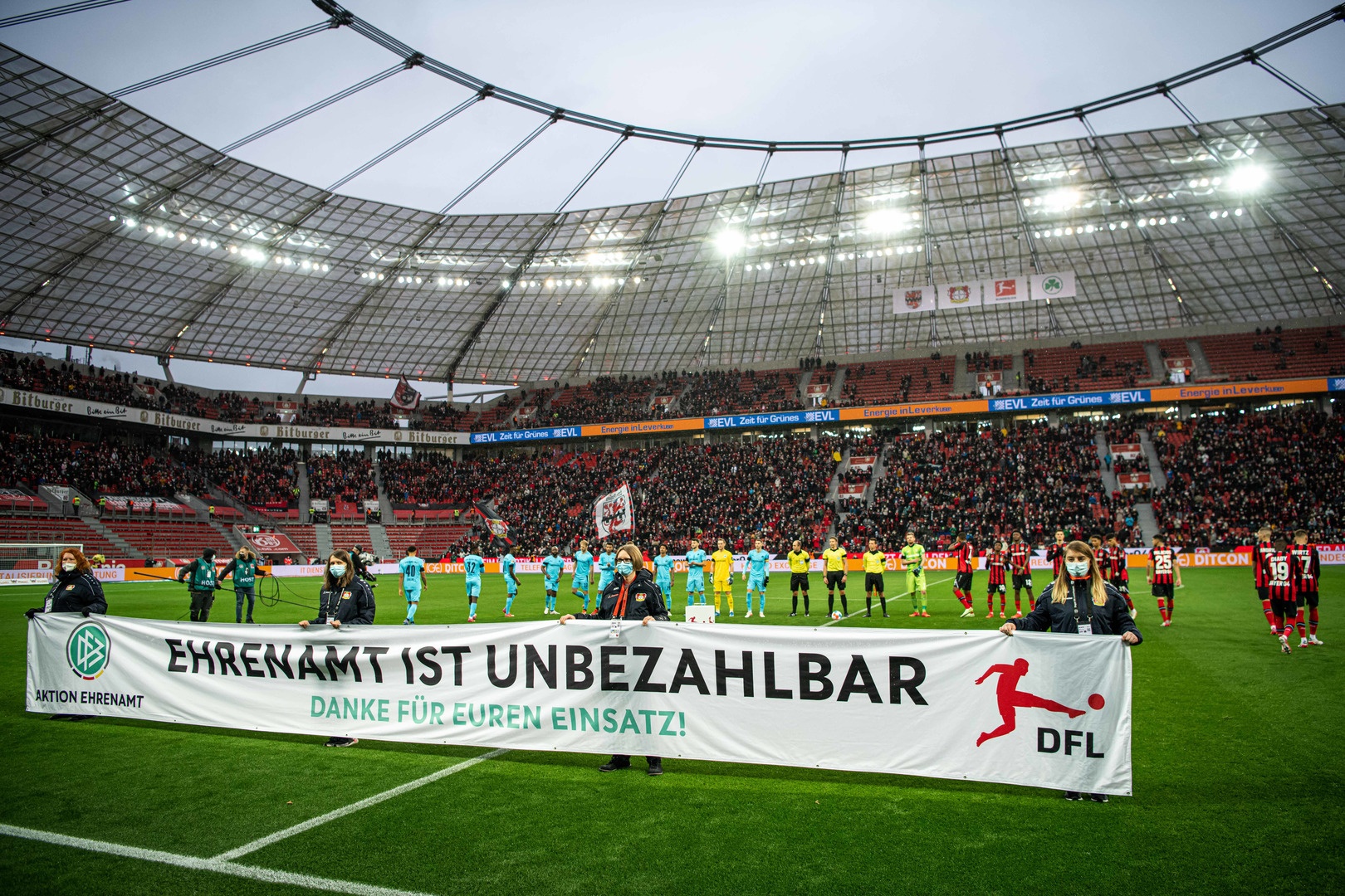 [{"clang_id":1,"value":"Fußballstadion mit Spielern und Betreuern auf dem Rasen. Ein Banner mit der Aufschrift \"Ehrenamt ist unbezahlbar. Danke für euren Einsatz!\" wird gehalten. Zuschauerreihen sind teilweise gefüllt."}]