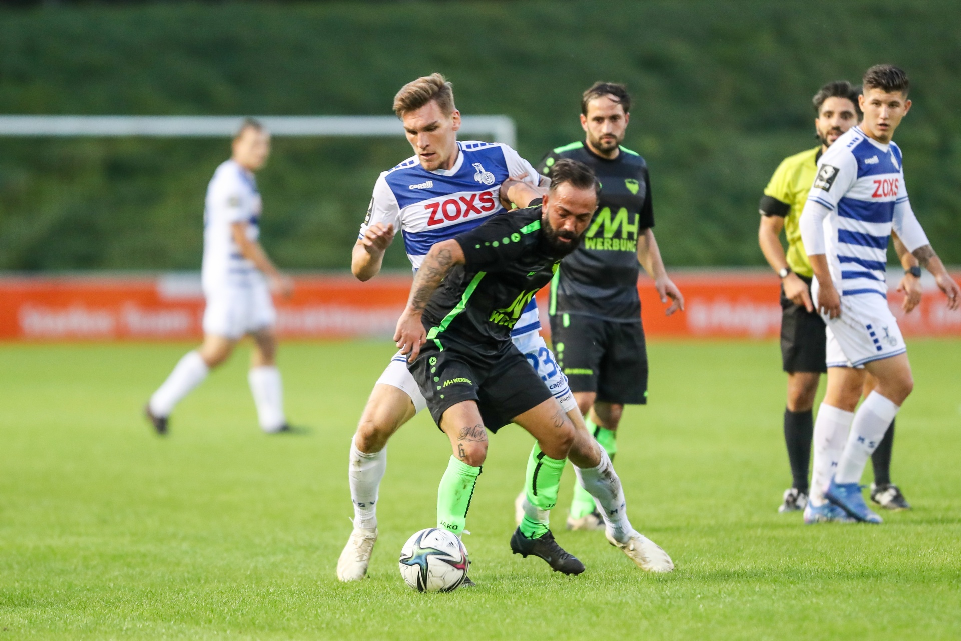 [{"clang_id":1,"value":"Fußballspiel: Zwei Spieler kämpfen um den Ball. Im Hintergrund weitere Spieler auf dem grünen Rasen."}]