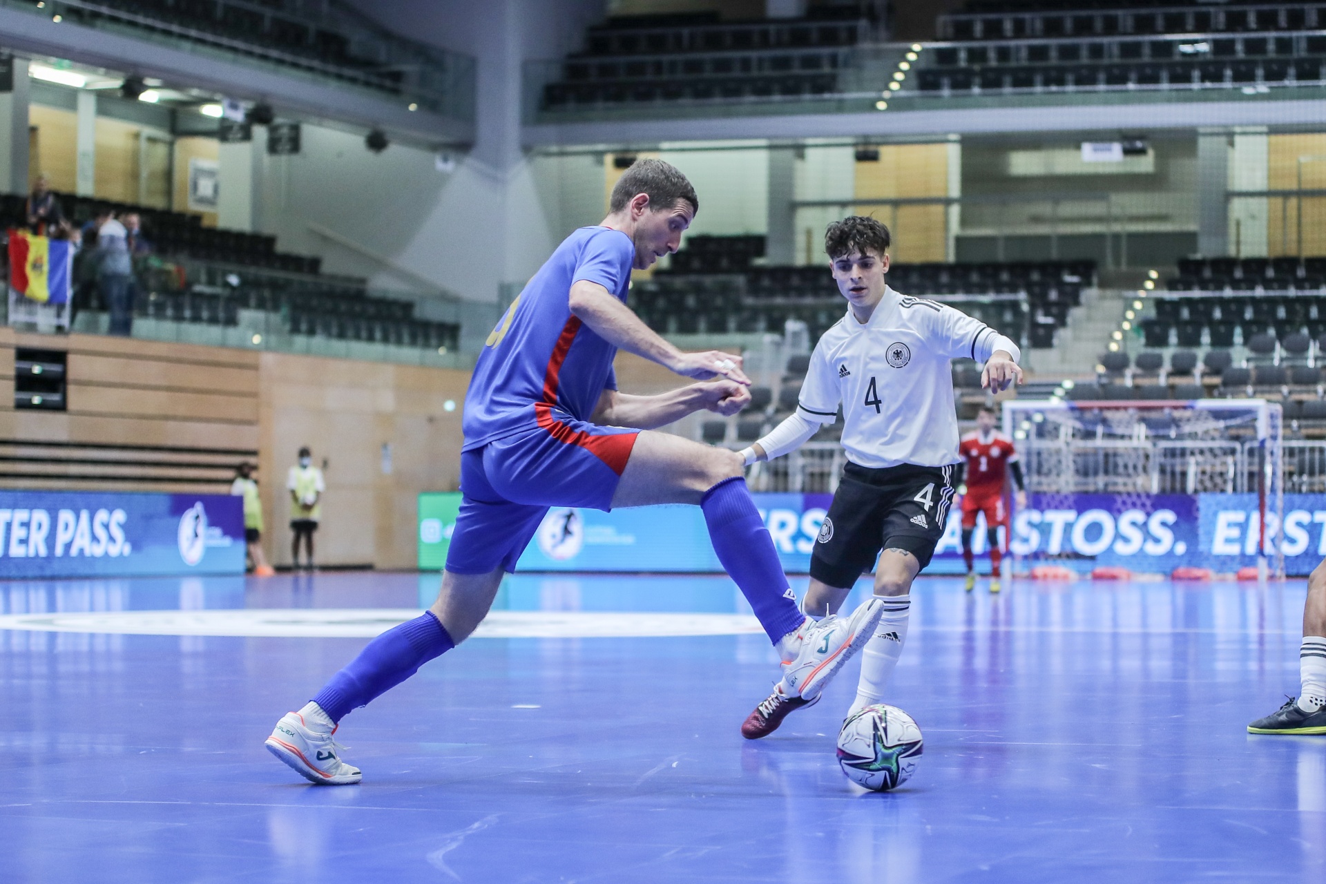 [{"clang_id":1,"value":"Futsalspiel: Spieler mit blauem Trikot versucht, Ball vom Spieler mit weiß-schwarzem Trikot (Nr. 4) zu erobern. Im Hintergrund Zuschauertribünen."}]