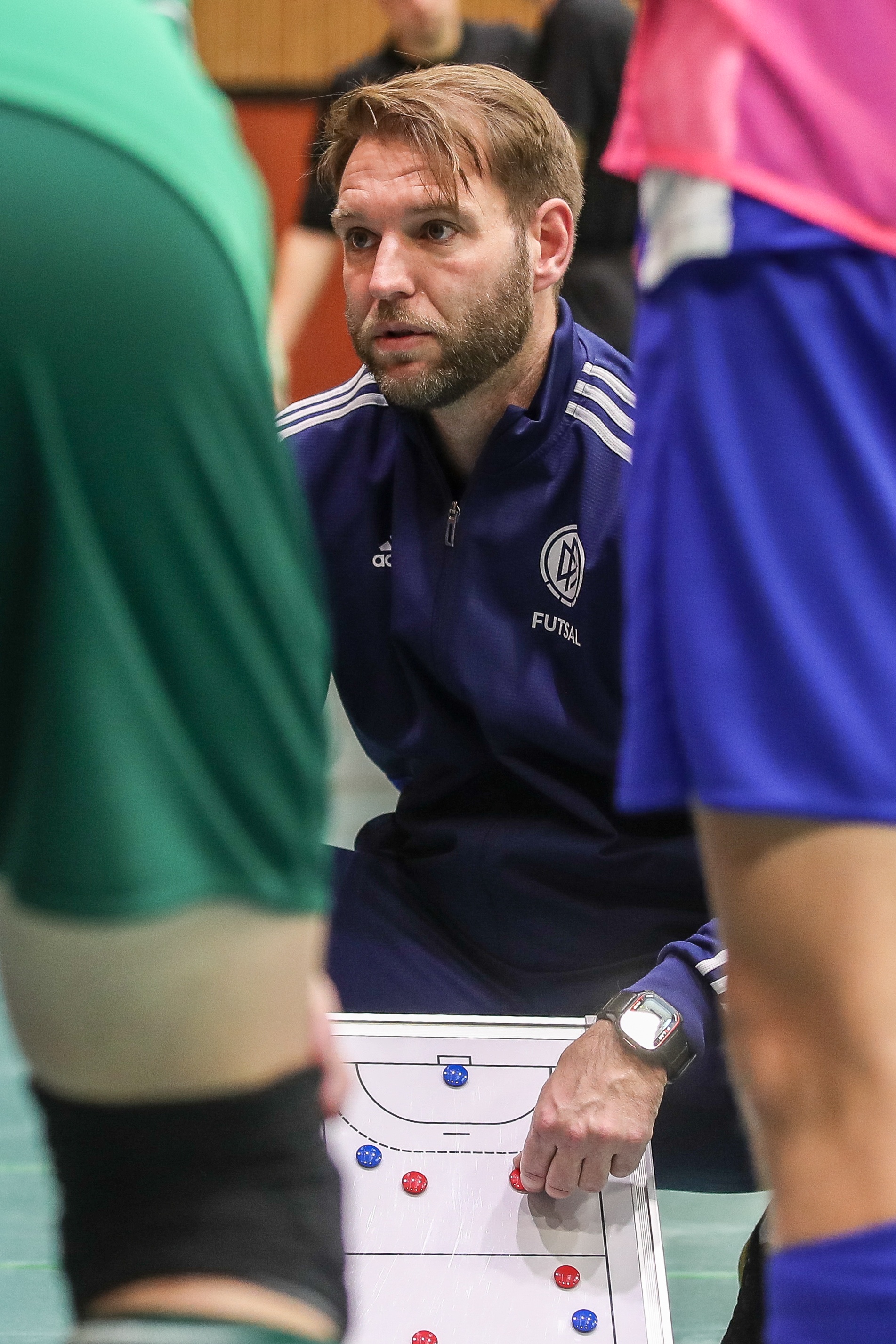 [{"clang_id":1,"value":"Futsal-Trainer bespricht Taktik mit Spielern am Spielfeldrand. Er zeigt auf ein kleines strategisches Whiteboard mit Spielaufstellung."}]