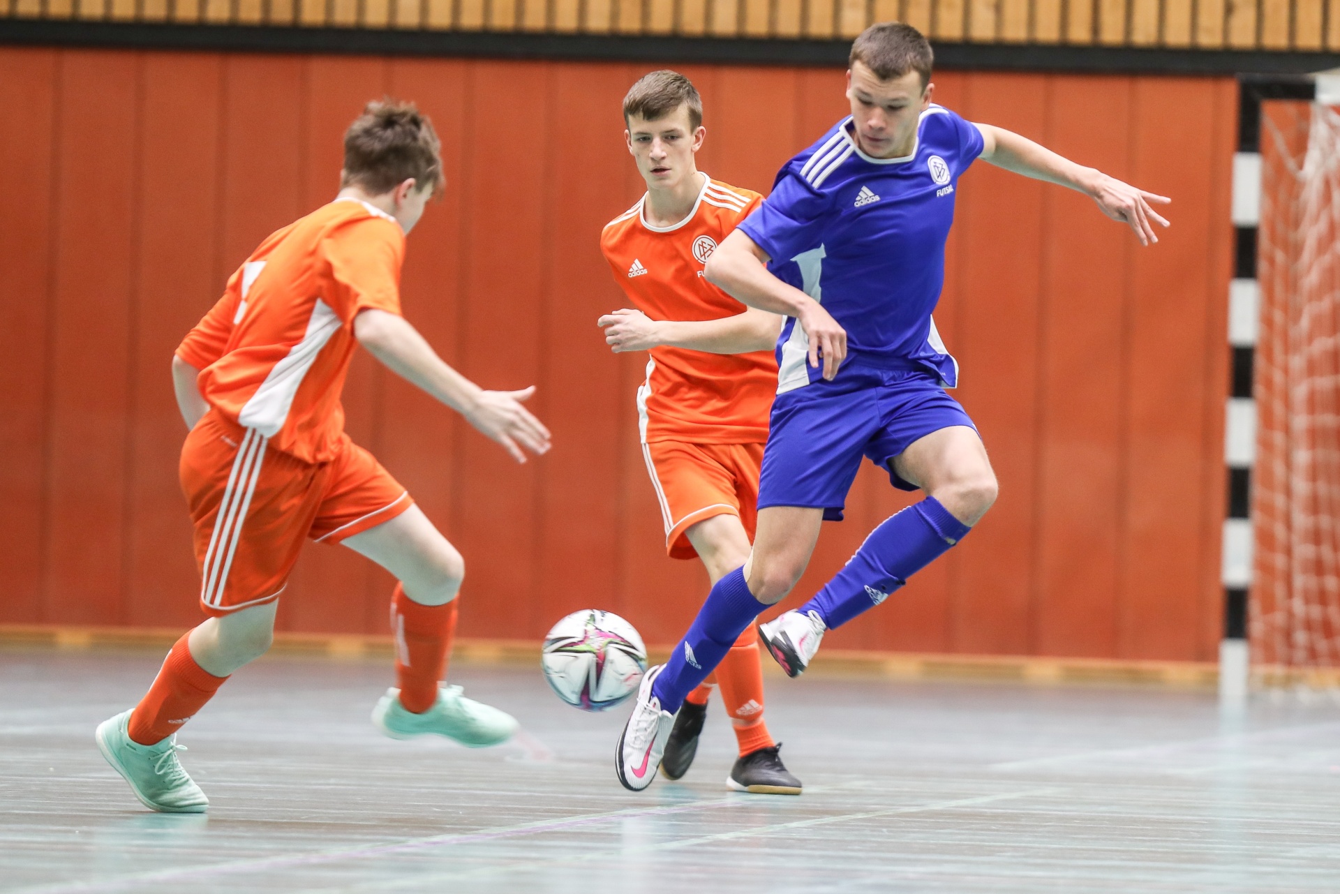 [{"clang_id":1,"value":"Drei Jugendliche spielen Futsal in einer Sporthalle. Ein Spieler in Blau dribbelt den Ball, zwei in Orange versuchen ihn zu blocken."}]