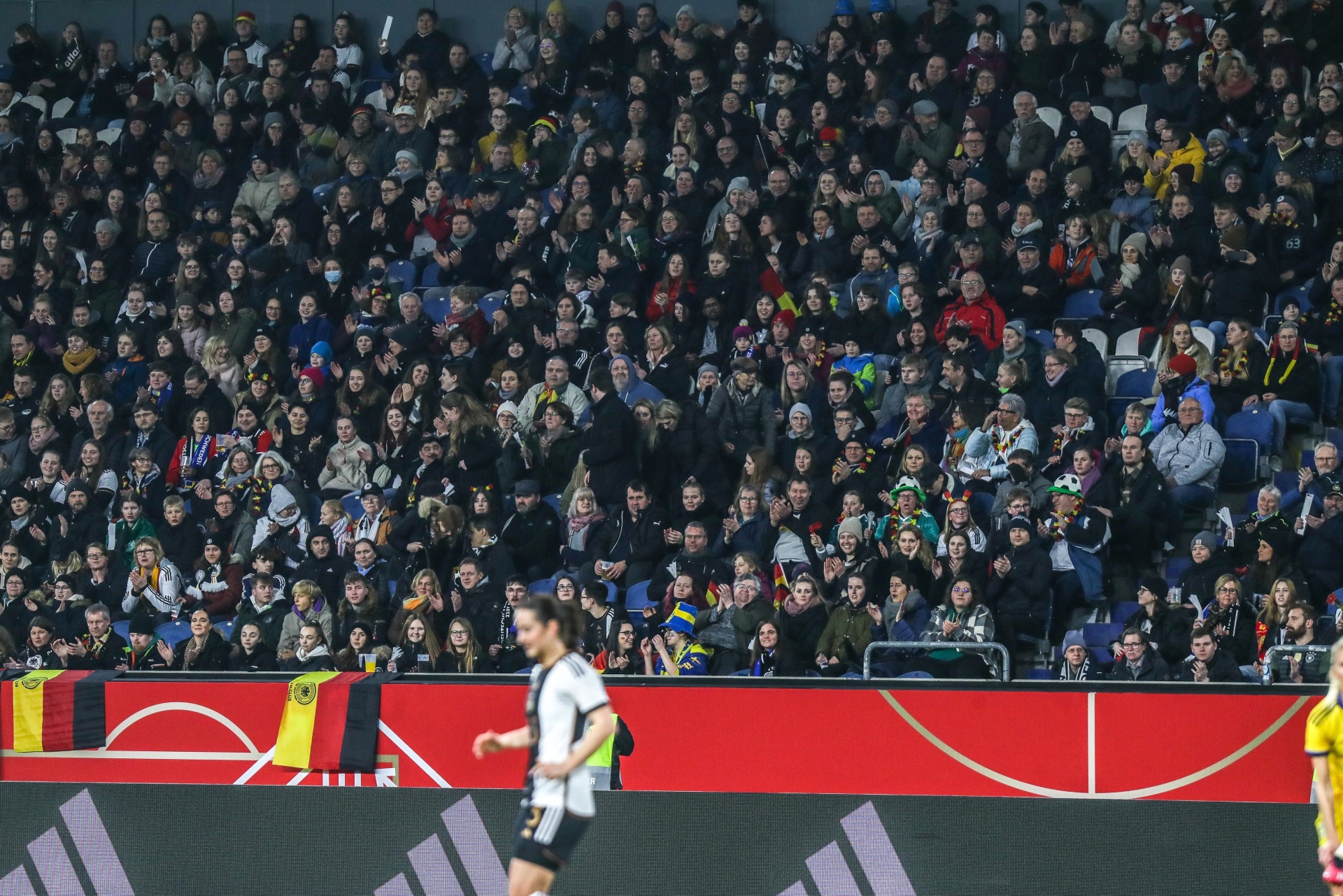 [{"clang_id":1,"value":"Fußballstadion gefüllt mit Zuschauern. Im Vordergrund ein roter Bereich mit Spieler in Schwarz-Weiß und einem Spieler in Gelb."}]