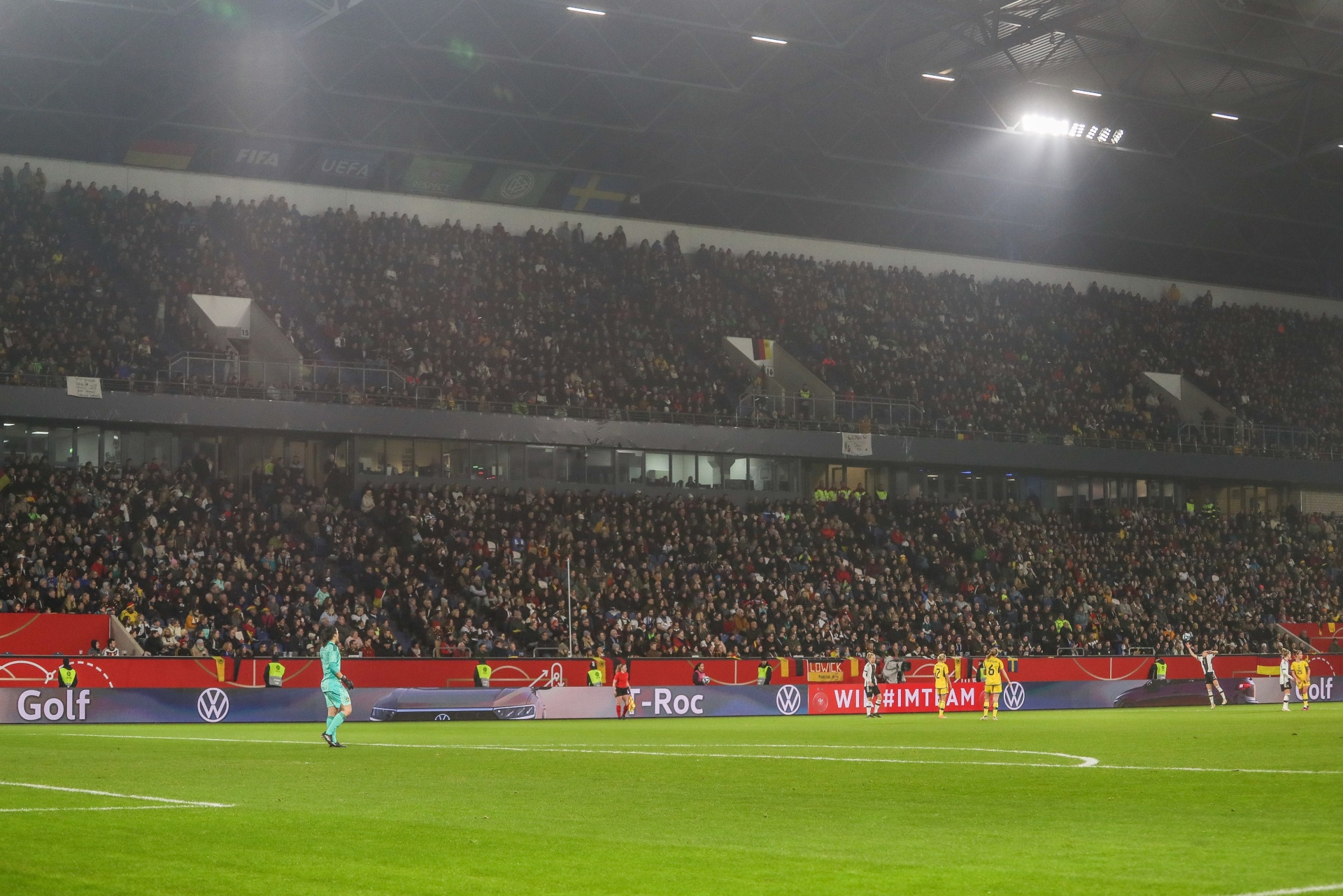 [{"clang_id":1,"value":"Fußballstadion bei Nacht, gefüllt mit Zuschauern. Spieler in roten Trikots auf grünem Rasen, umgeben von Werbebanden. Flutlicht."}]