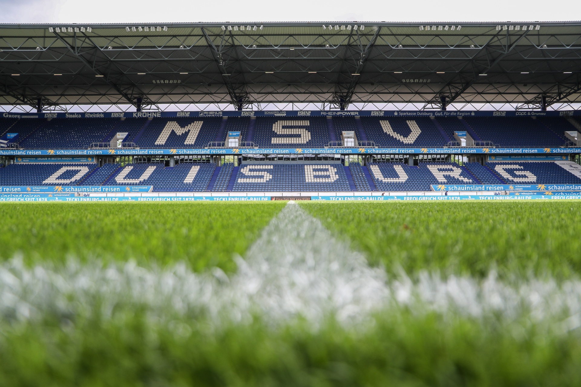 [{"clang_id":1,"value":"Fußballstadion: Tribünen mit blauem Schriftzug \"MSV Duisburg\". Hintergrund ist der grüne Rasen des Spielfelds und das Stadiondach."}]