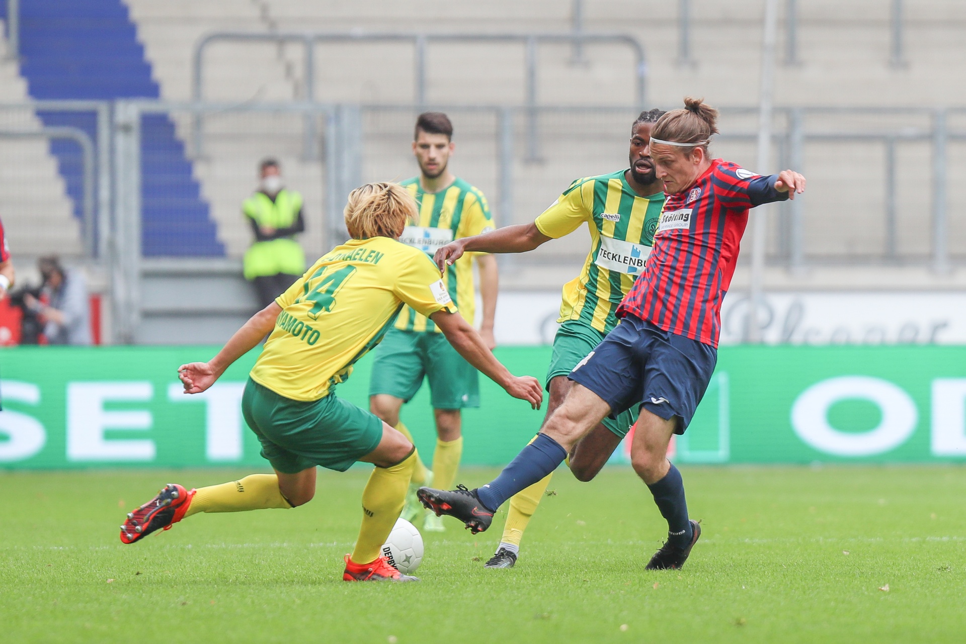 [{"clang_id":1,"value":"Zwei Fußballspieler kämpfen um den Ball. Ein Spieler in rotem und blauem Trikot tritt den Ball, ein Spieler in grünem Trikot versucht ihn zu blocken. Stadion im Hintergrund."}]