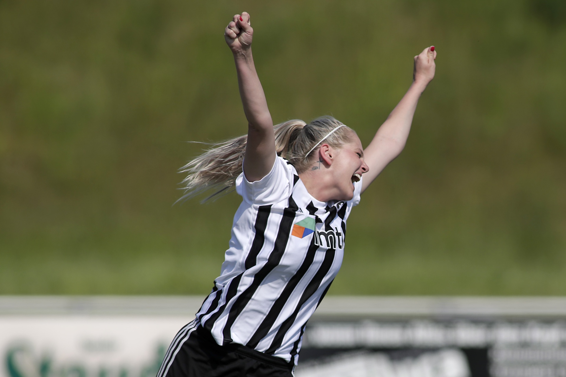 [{"clang_id":1,"value":"Frau feiert auf Fußballfeld mit erhobenen Armen. Sie trägt gestreiftes Trikot und kurze Hose. Hintergrund ist ein grüner Rasen."}]