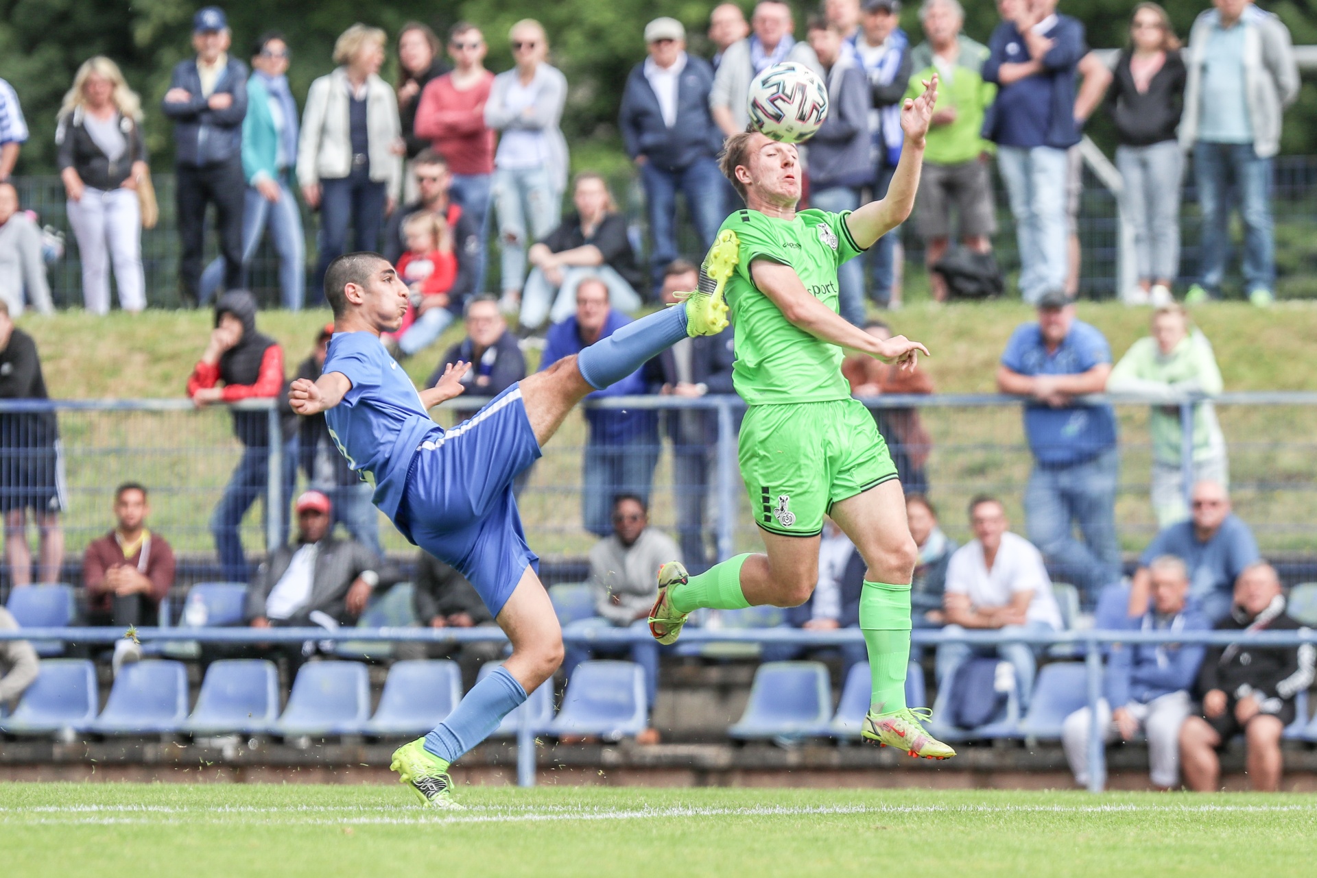 [{"clang_id":1,"value":"Zwei Fußballspieler springen in der Luft, um den Ball zu köpfen. Im Hintergrund Zuschauer auf einer Tribüne. Rasenplatz."}]