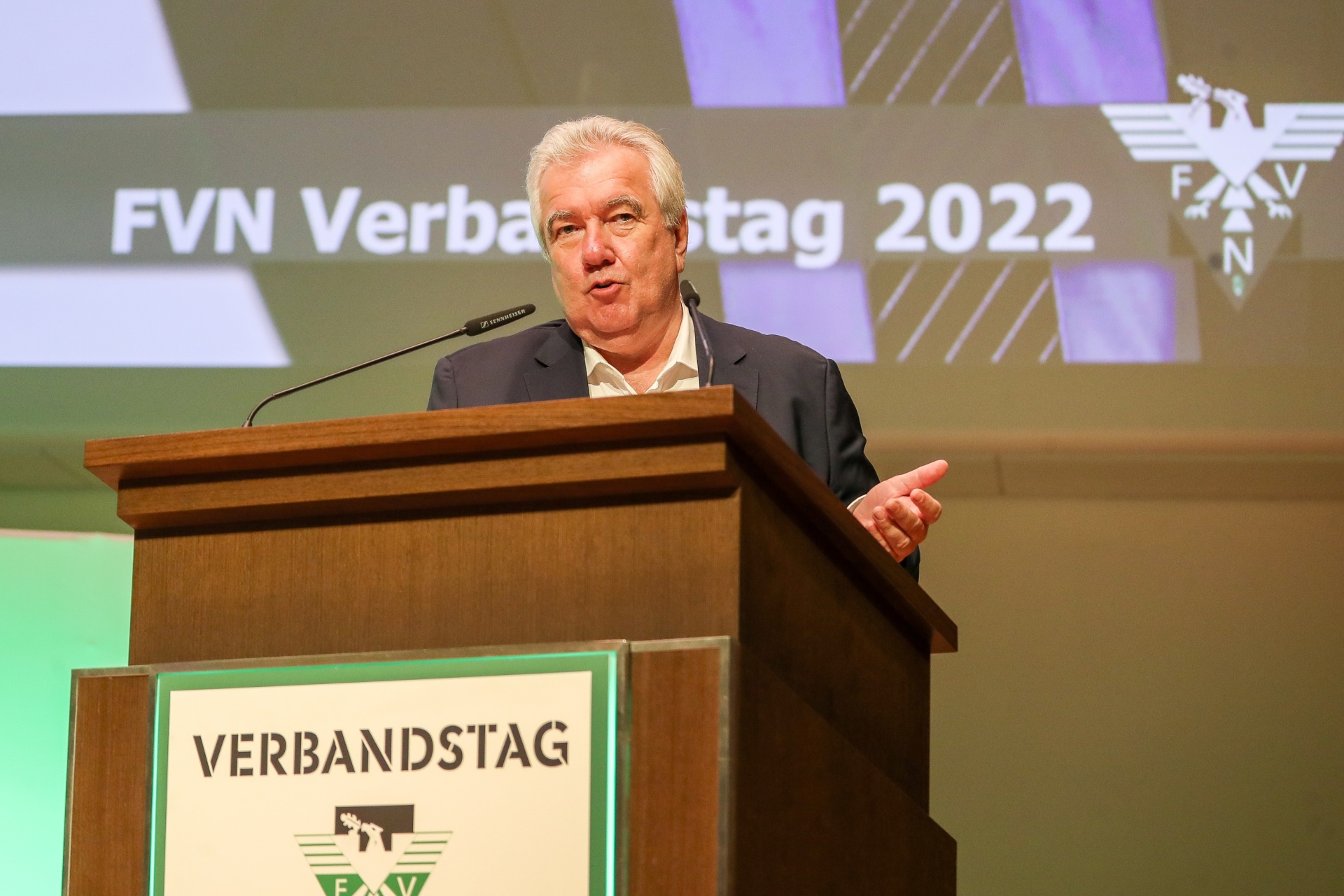 [{"clang_id":1,"value":"Mann am Rednerpult vor Publikum. Hintergrund: Banner \"FVN Verbandstag 2022\". Mann trägt Anzug, hält Rede."}]